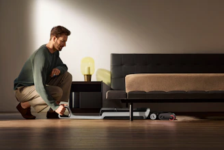 Man vacuuming under a bed with a robot vacuum