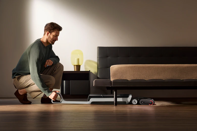 Man vacuuming under a bed with a robot vacuum