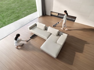 Two women cleaning a modern living room with vacuum cleaners.