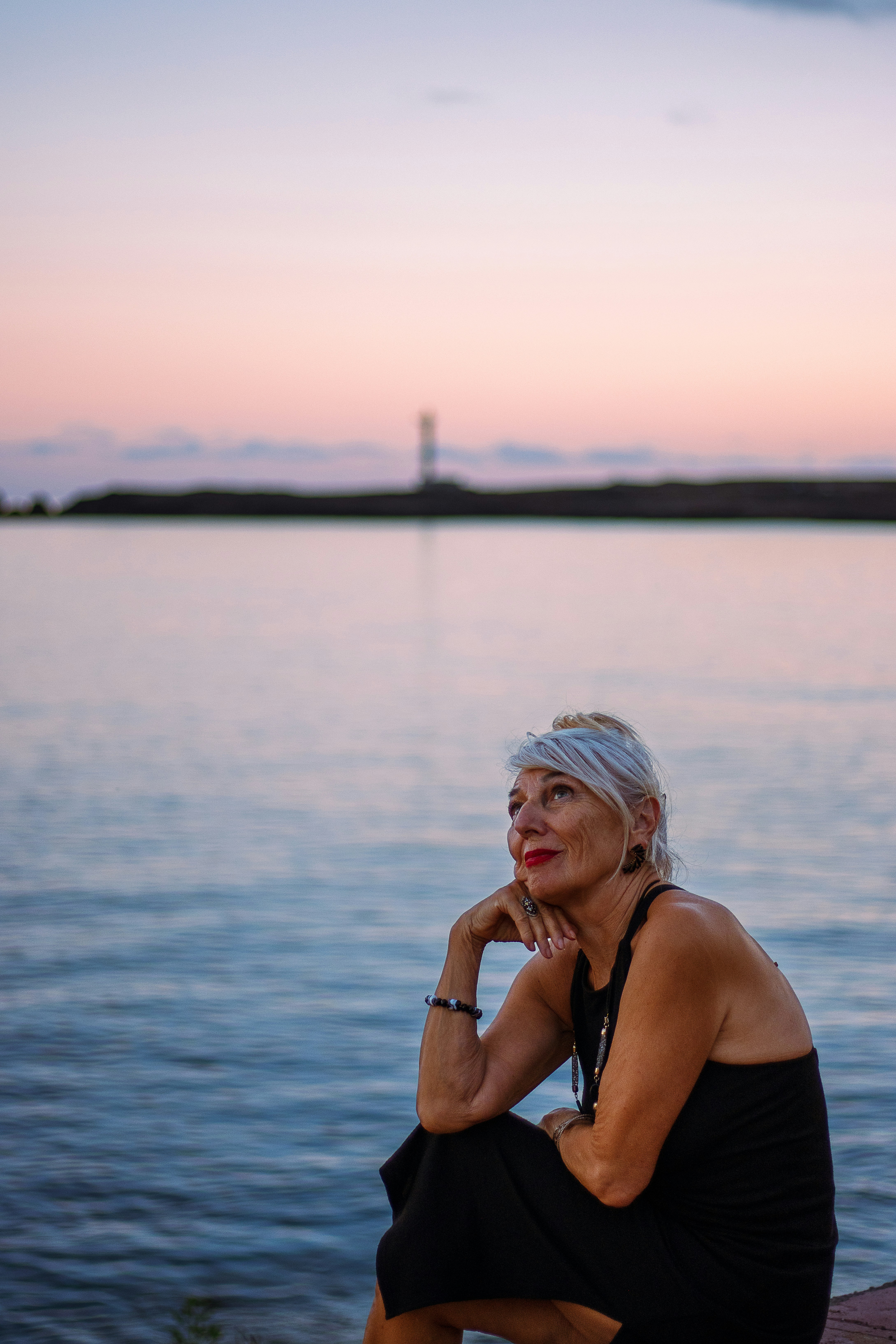 Woman looking up at a pastel sunset over water