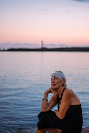 Woman looking up at a pastel sunset over water