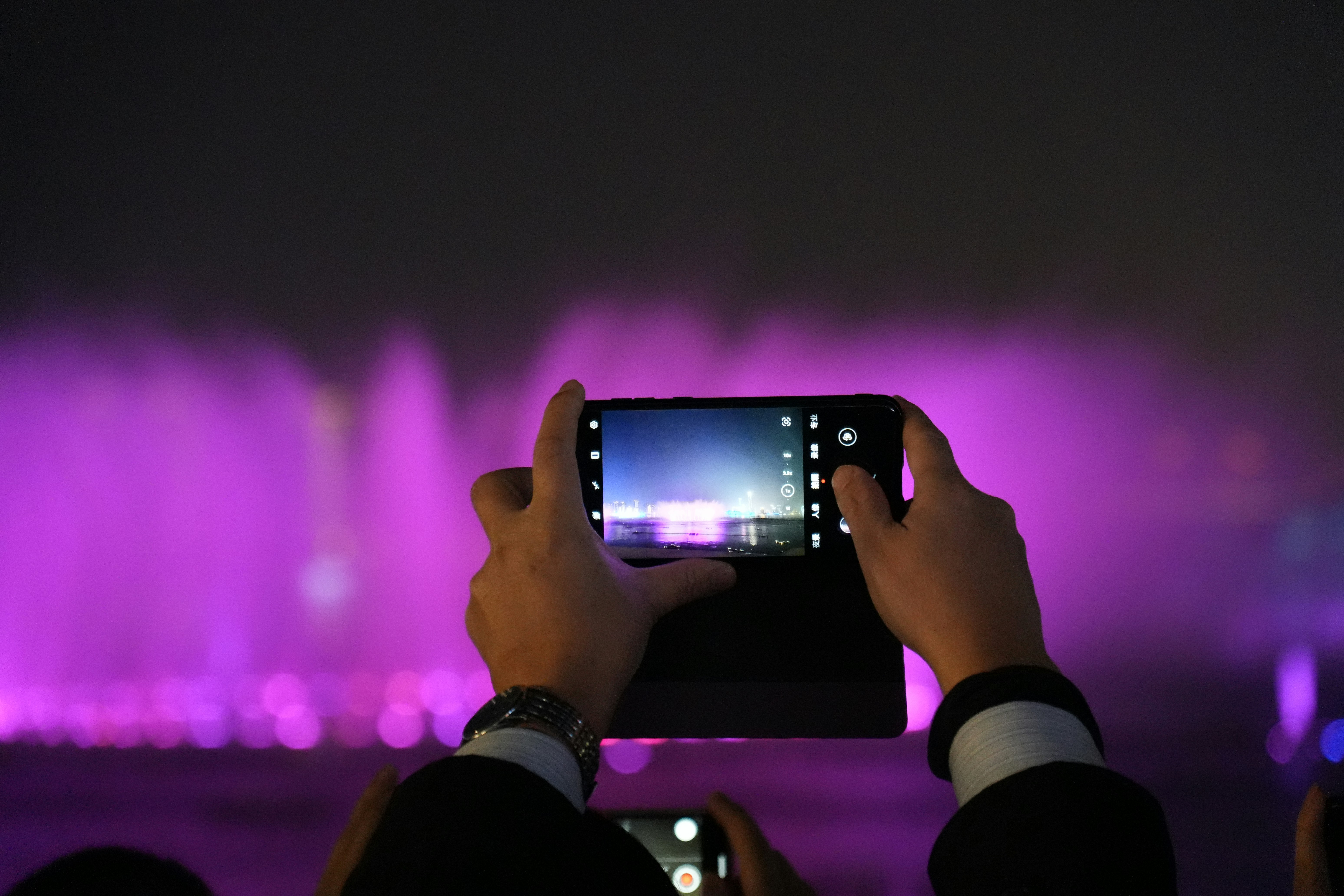 Mãos segurando o smartphone gravando um show de fonte roxa.