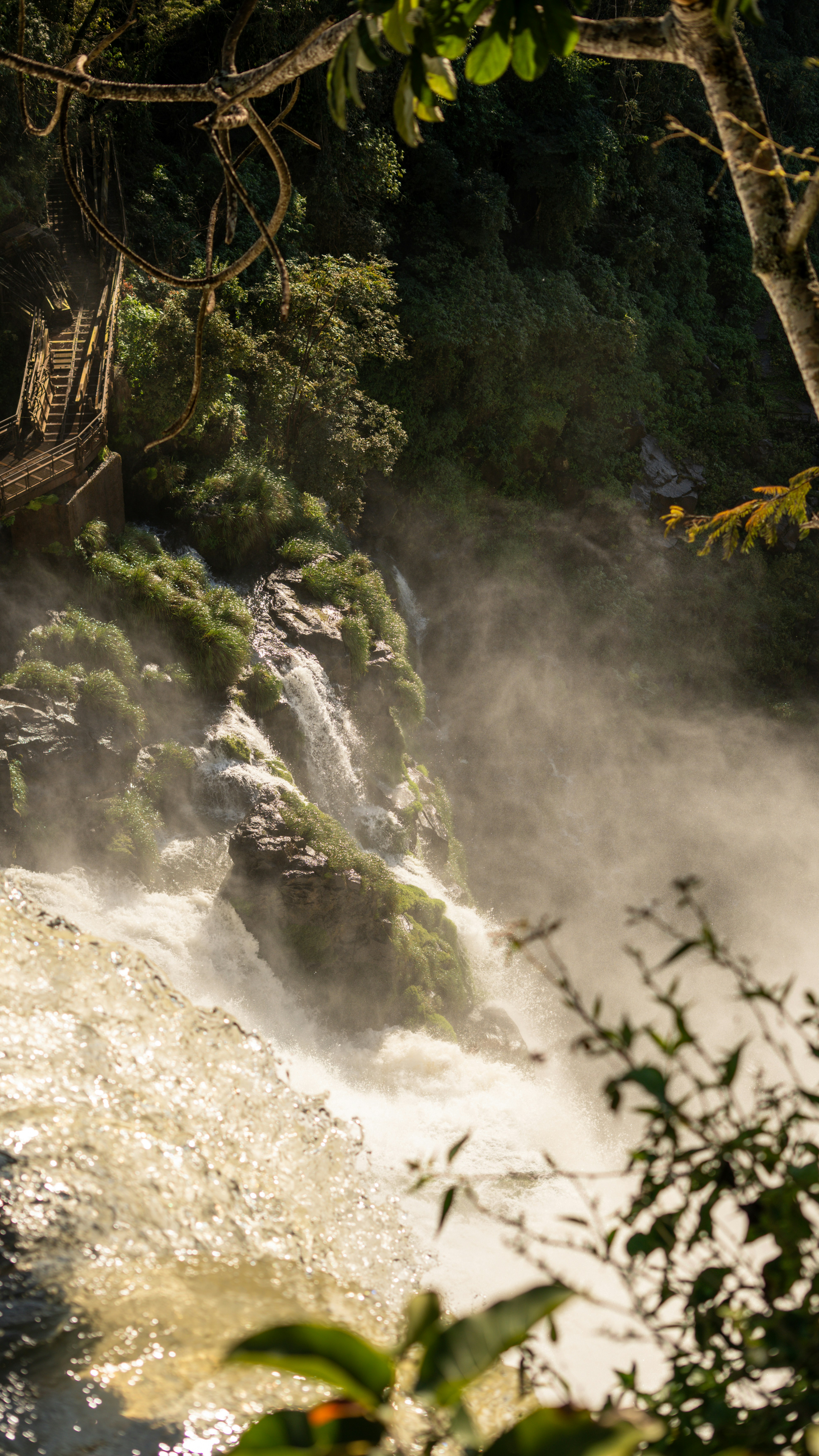 Misty waterfall cascading down mossy rocks with wooden stairs.
