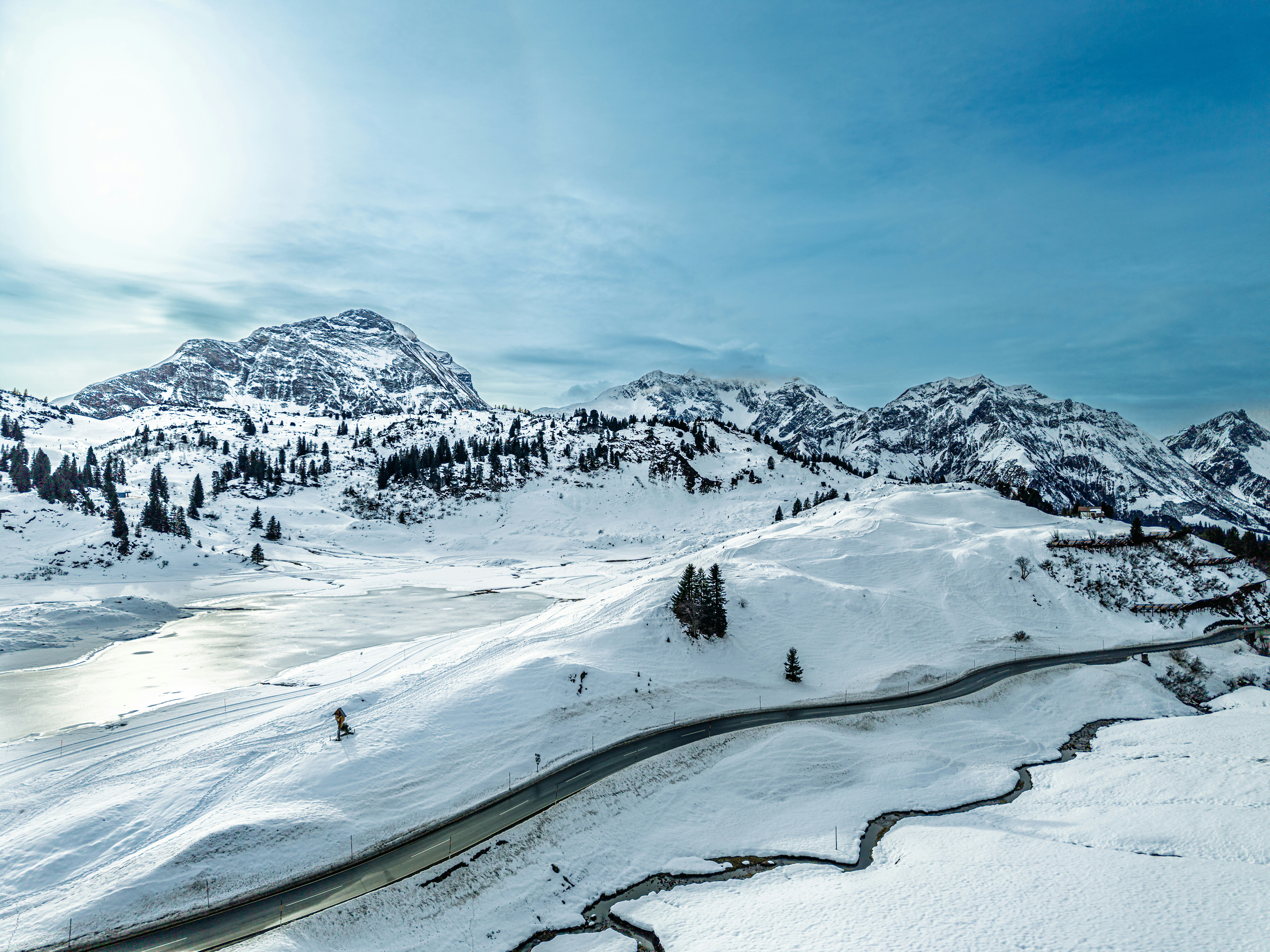 Snow-covered mountains with a winding road and frozen lake.