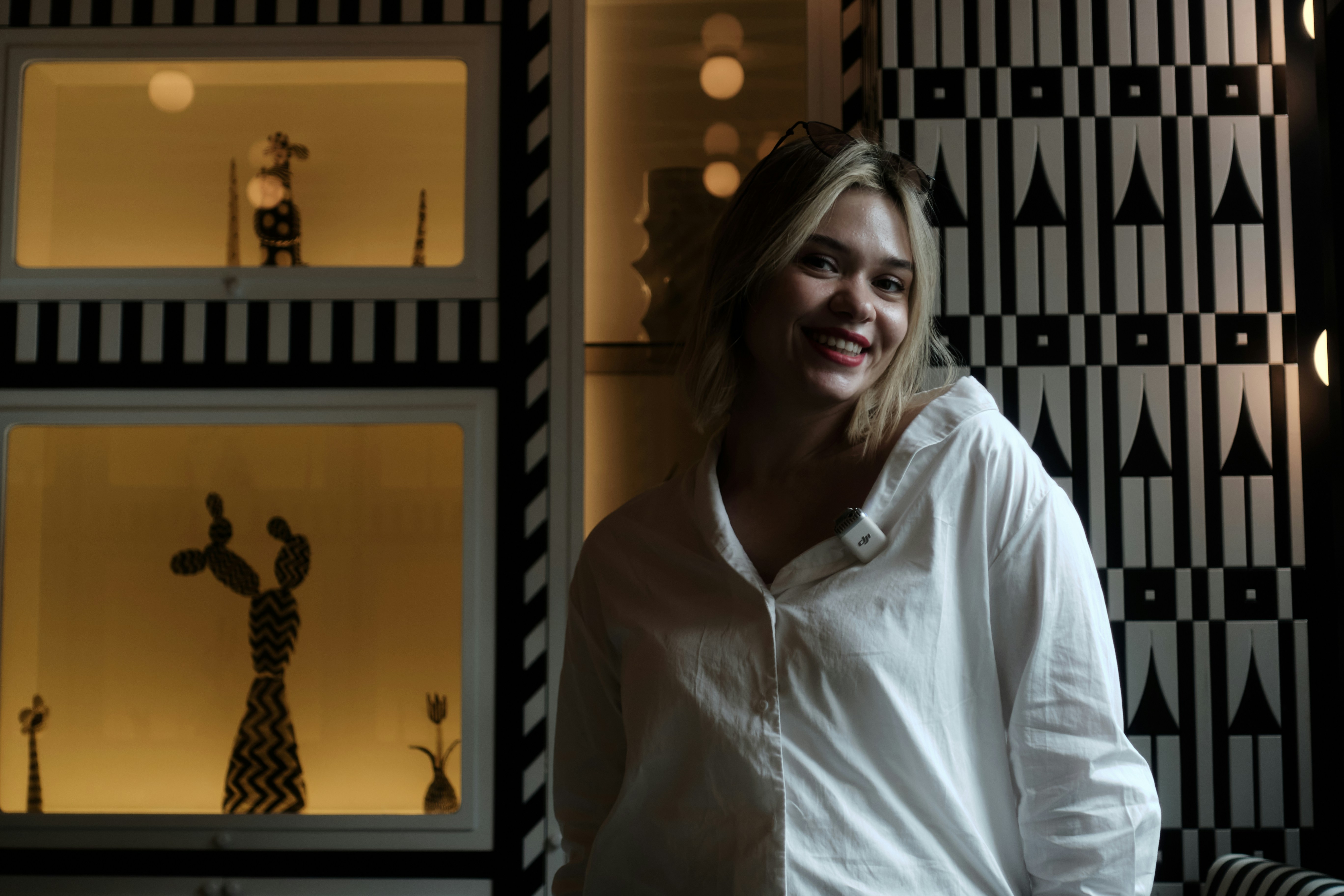 A young woman smiles in a room with patterned walls.