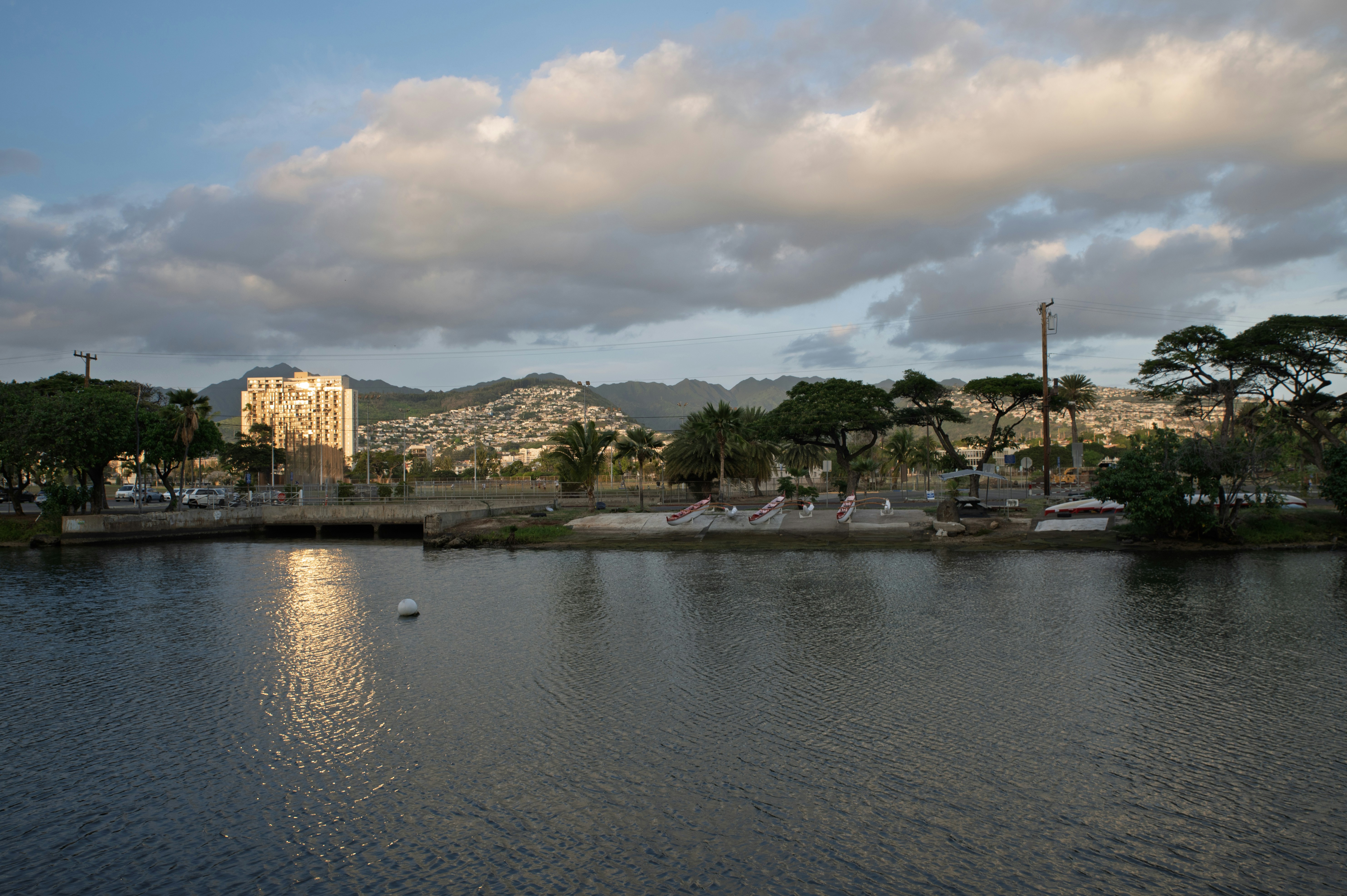 Calm water reflects sunlight near buildings and trees.