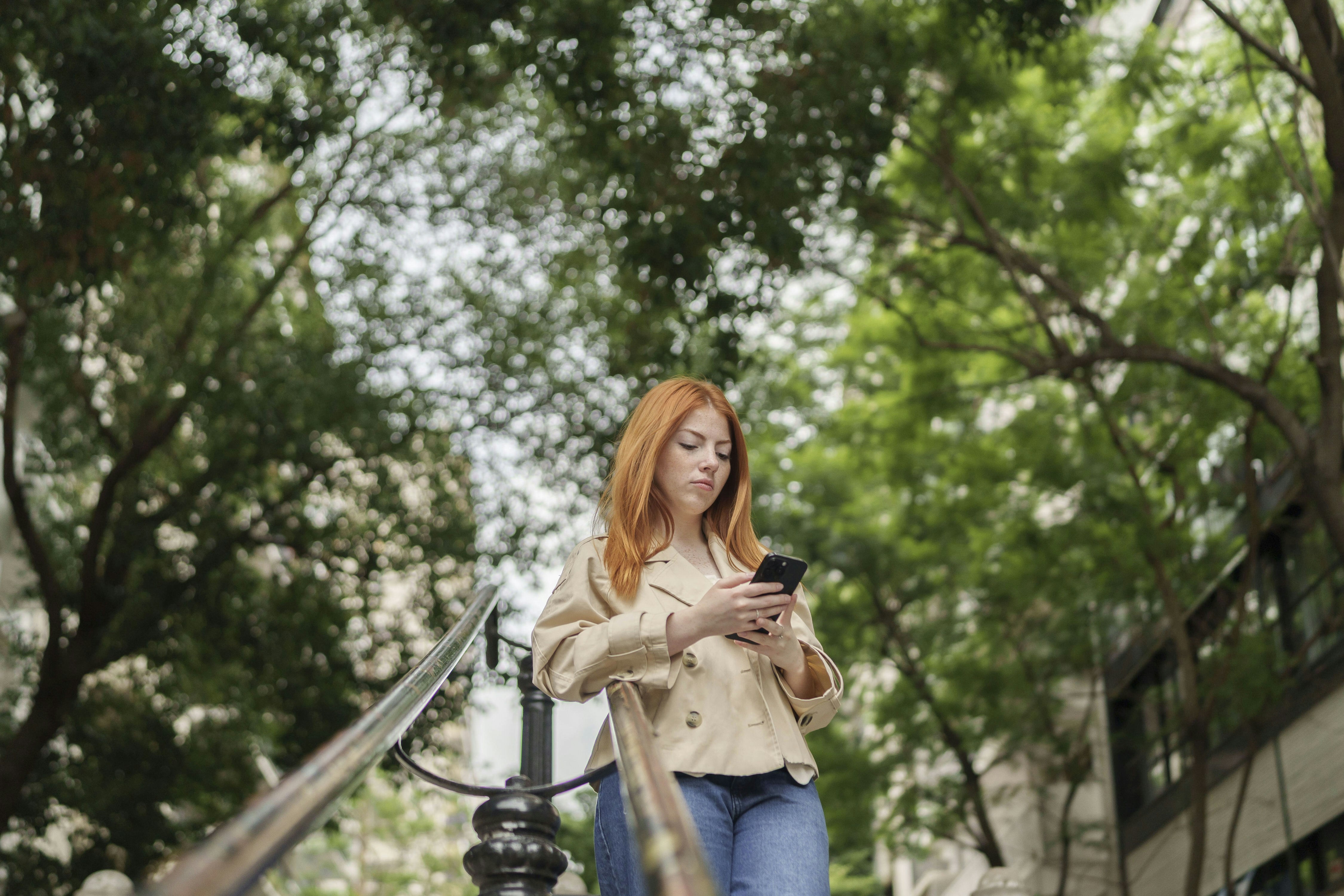 Mulher de cabelo ruivo usando um smartphone ao ar livre.