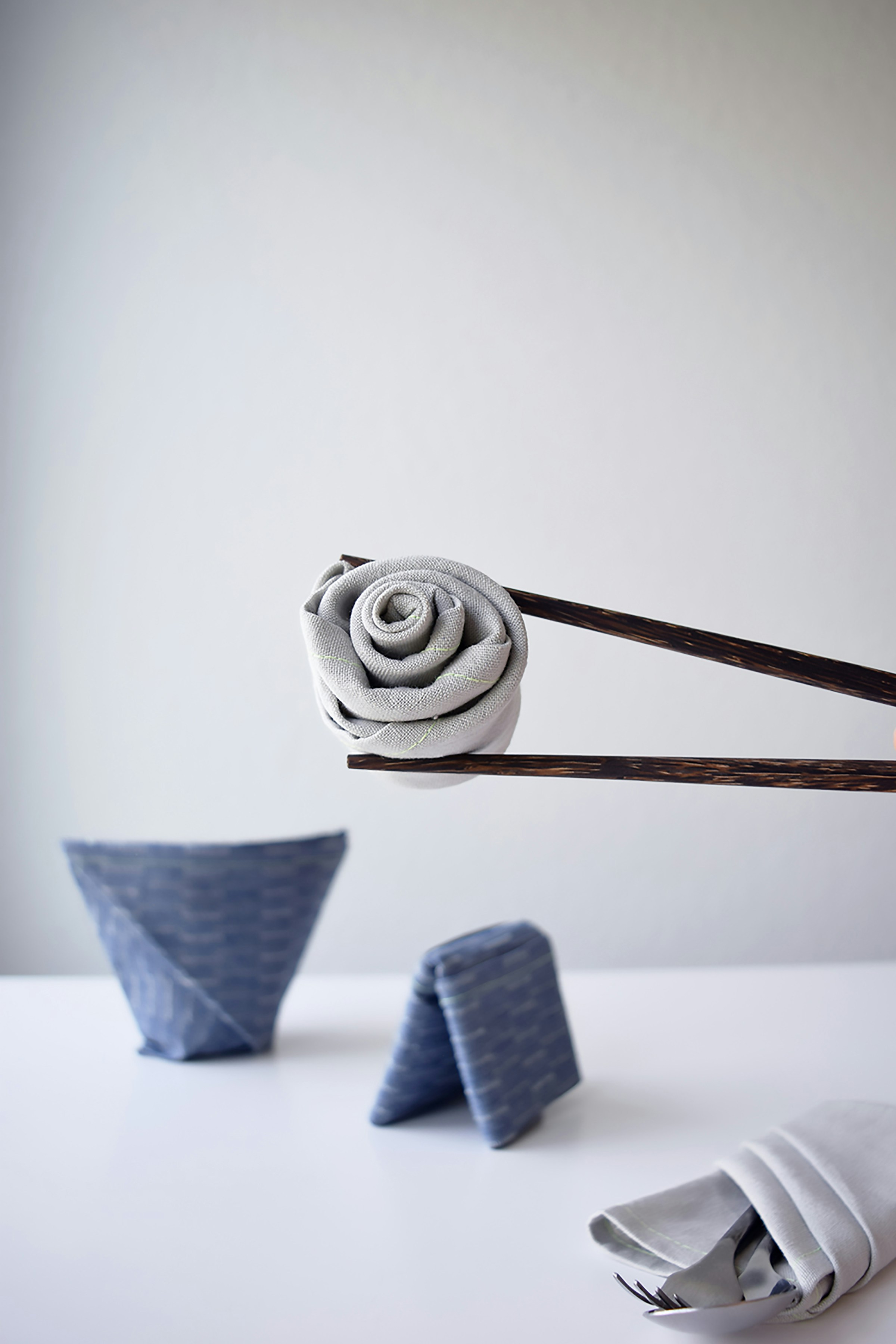 Chopsticks holding a rolled cloth napkin shaped like a rose.