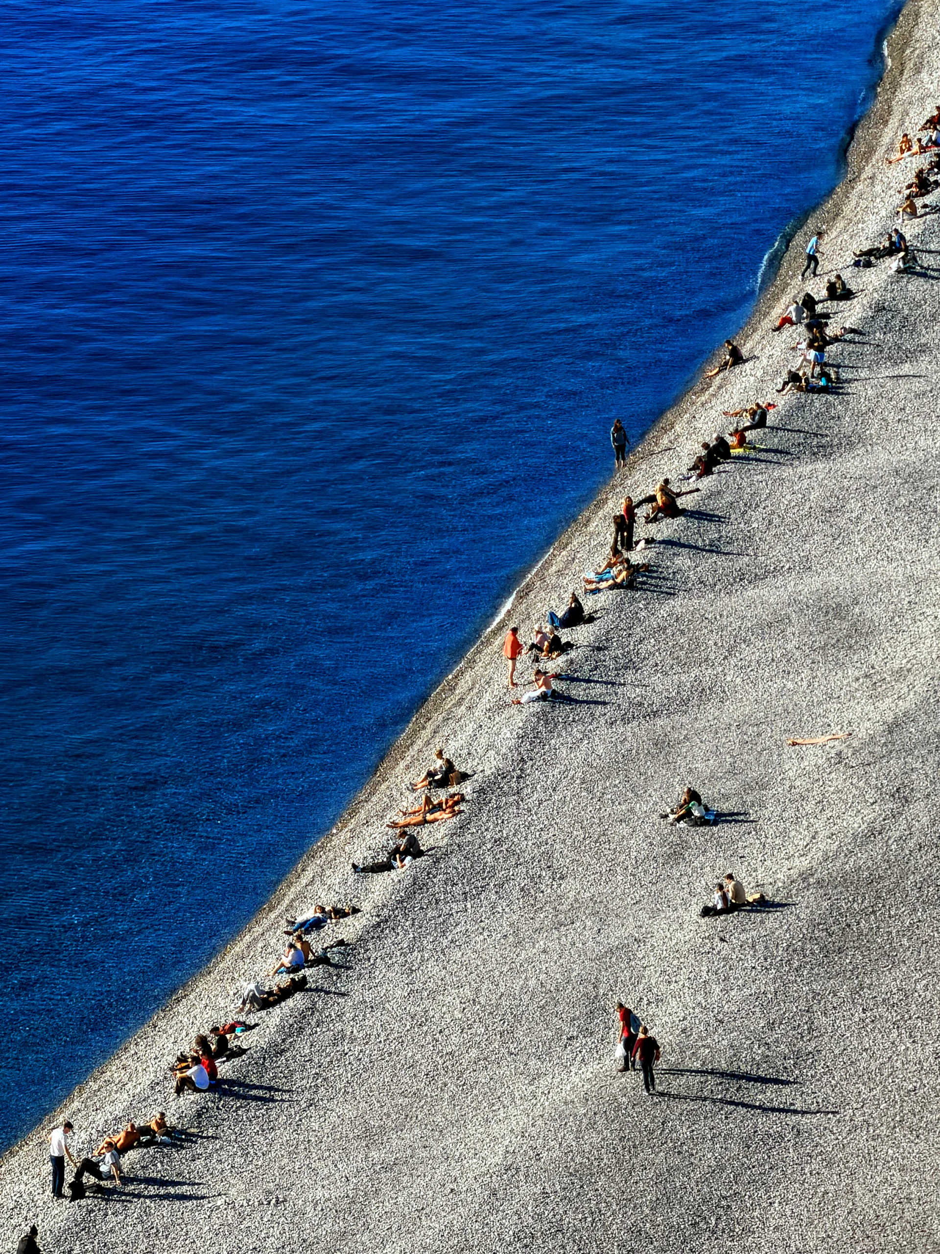 People sunbathing on a pebble beach next to blue ocean.