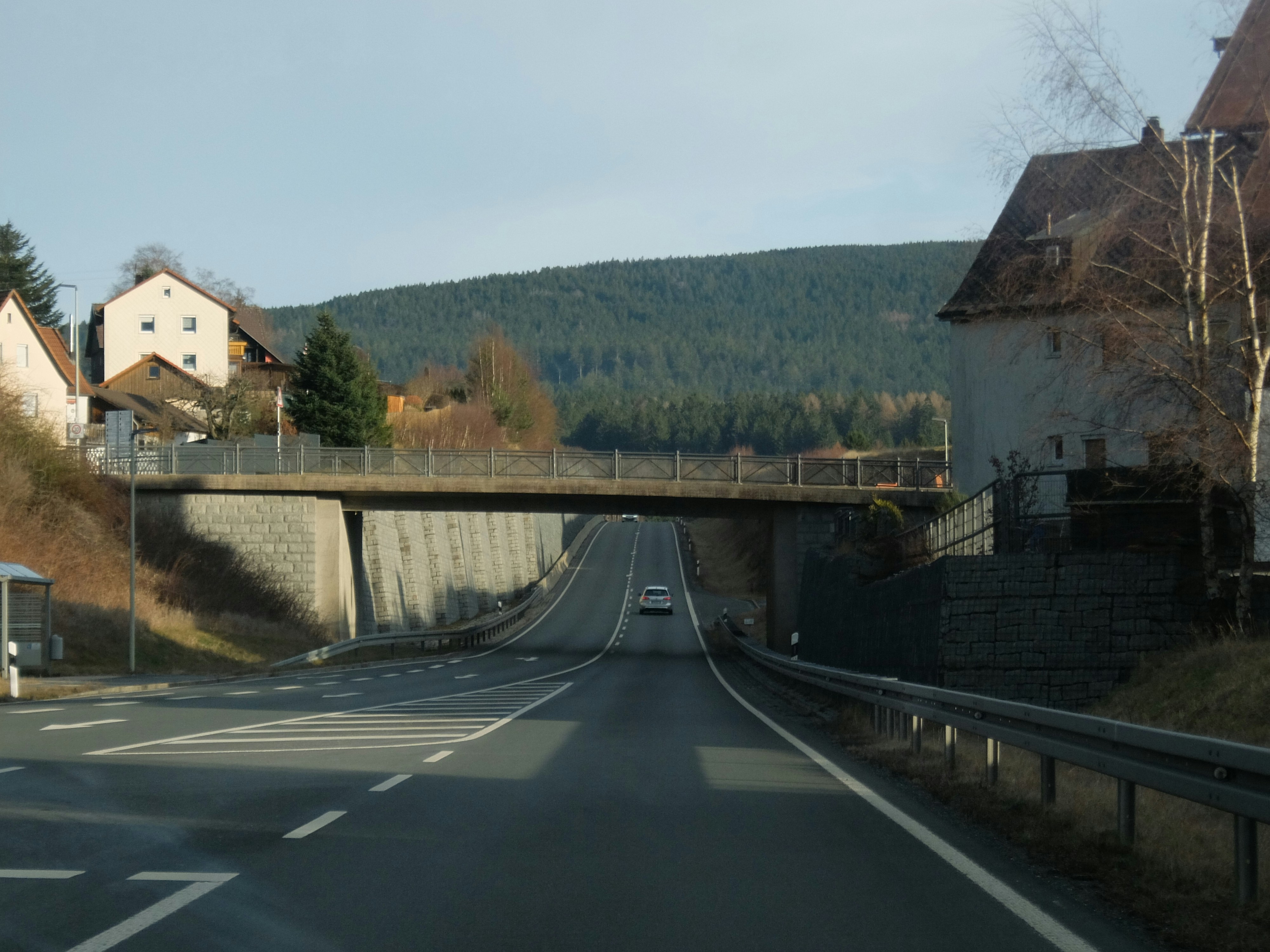 A road passes under a bridge with houses nearby.