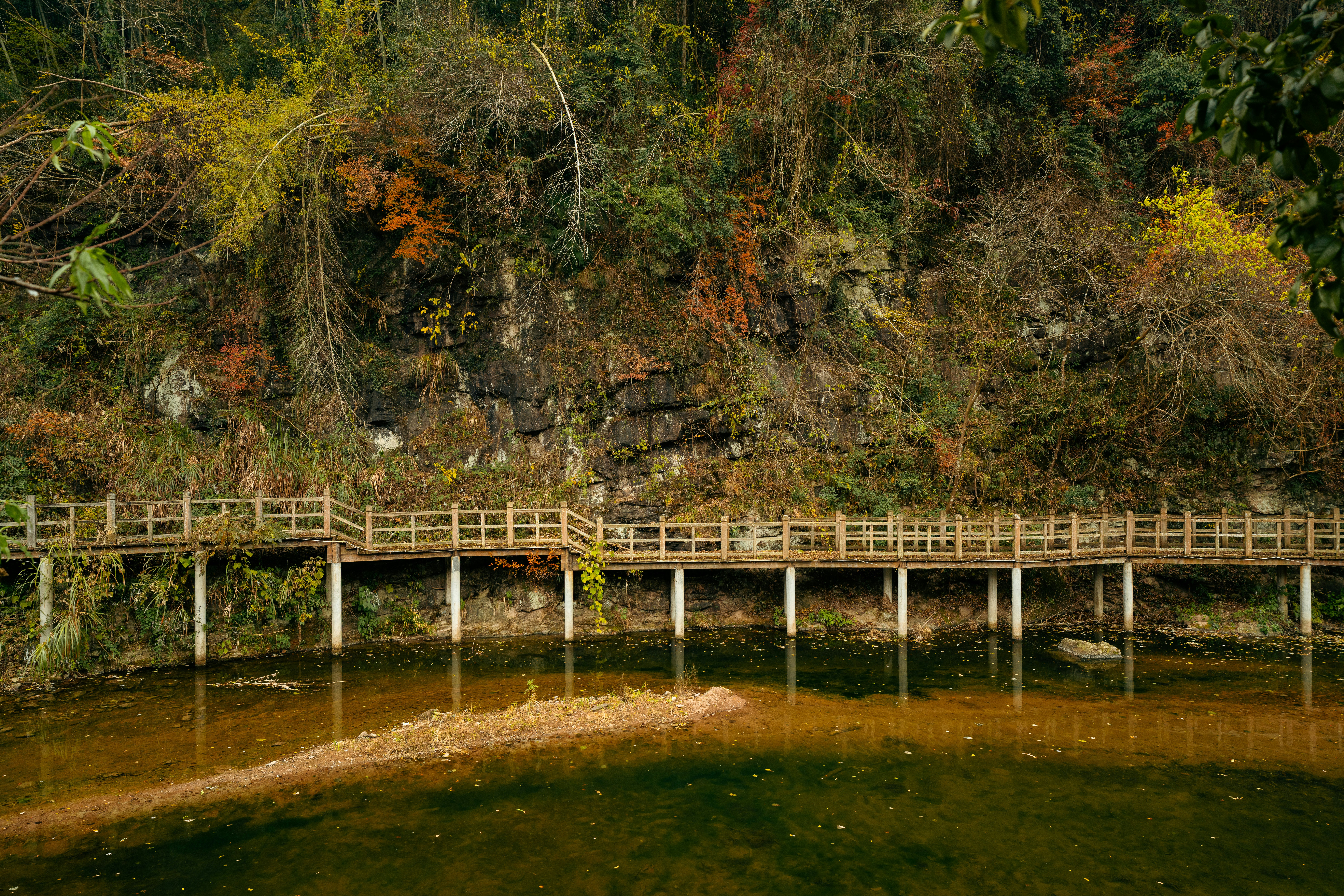Wooden boardwalk along a rocky hillside with autumn foliage.