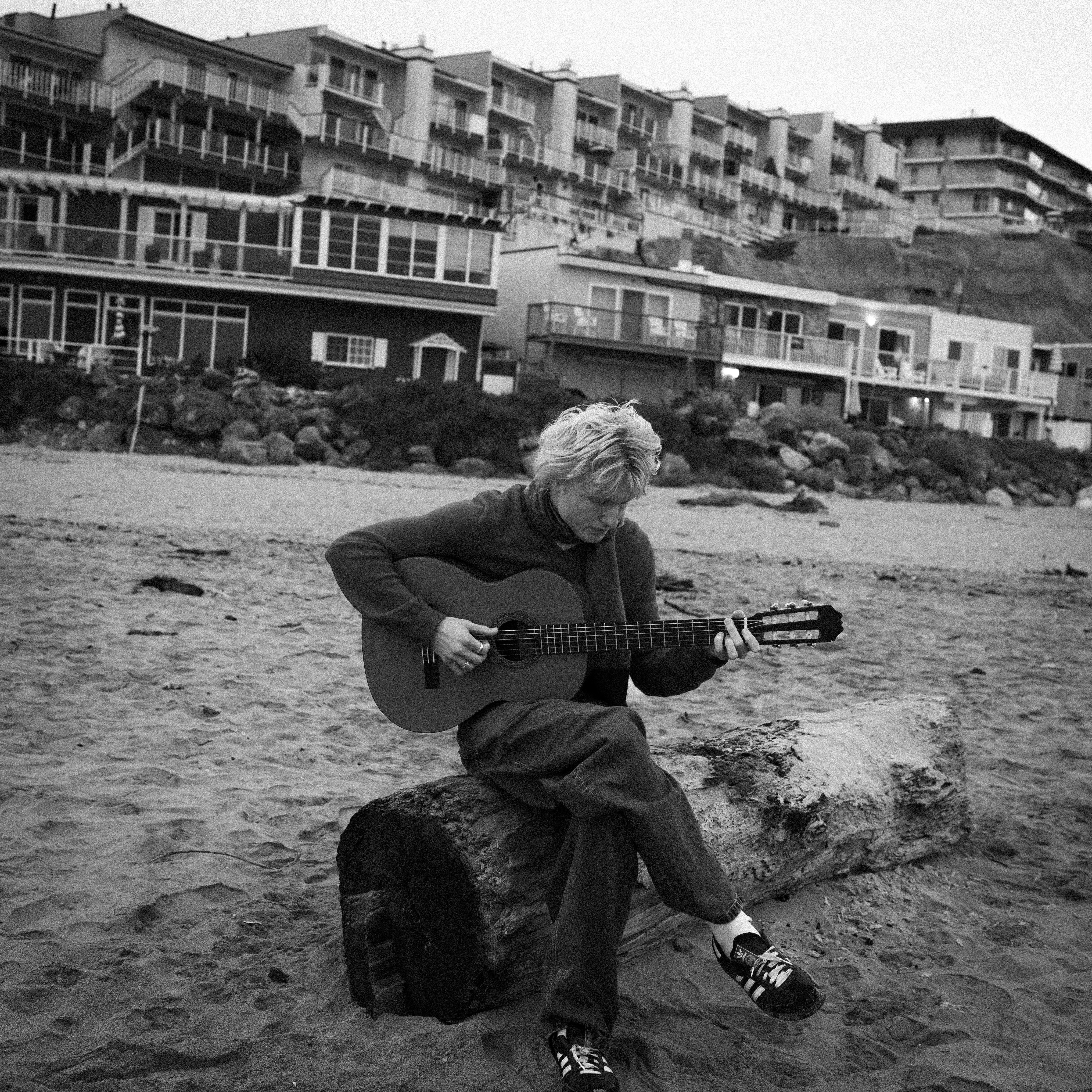 Woman playing guitar on a log at the beach.