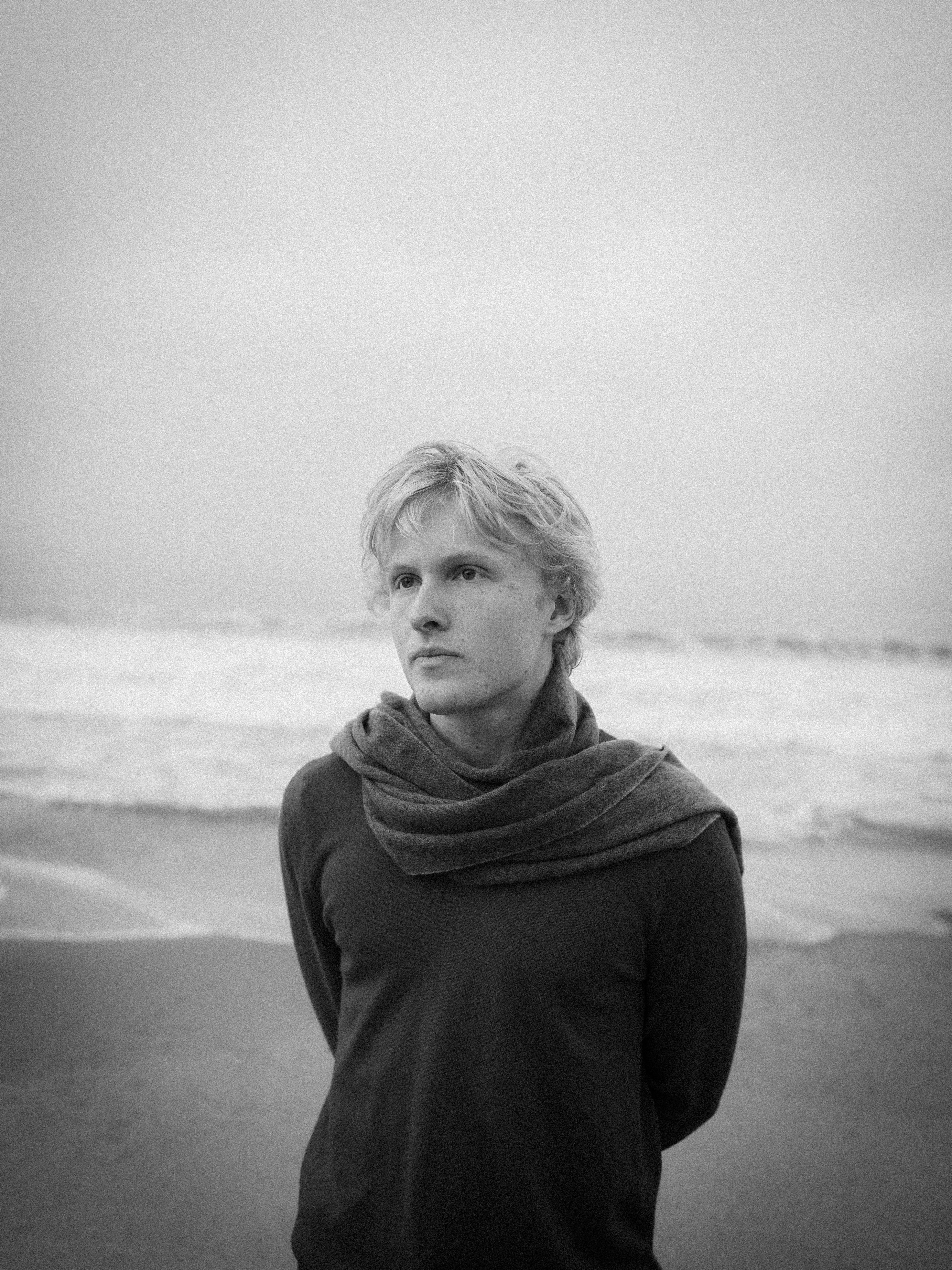 Man with scarf on beach looking out to sea
