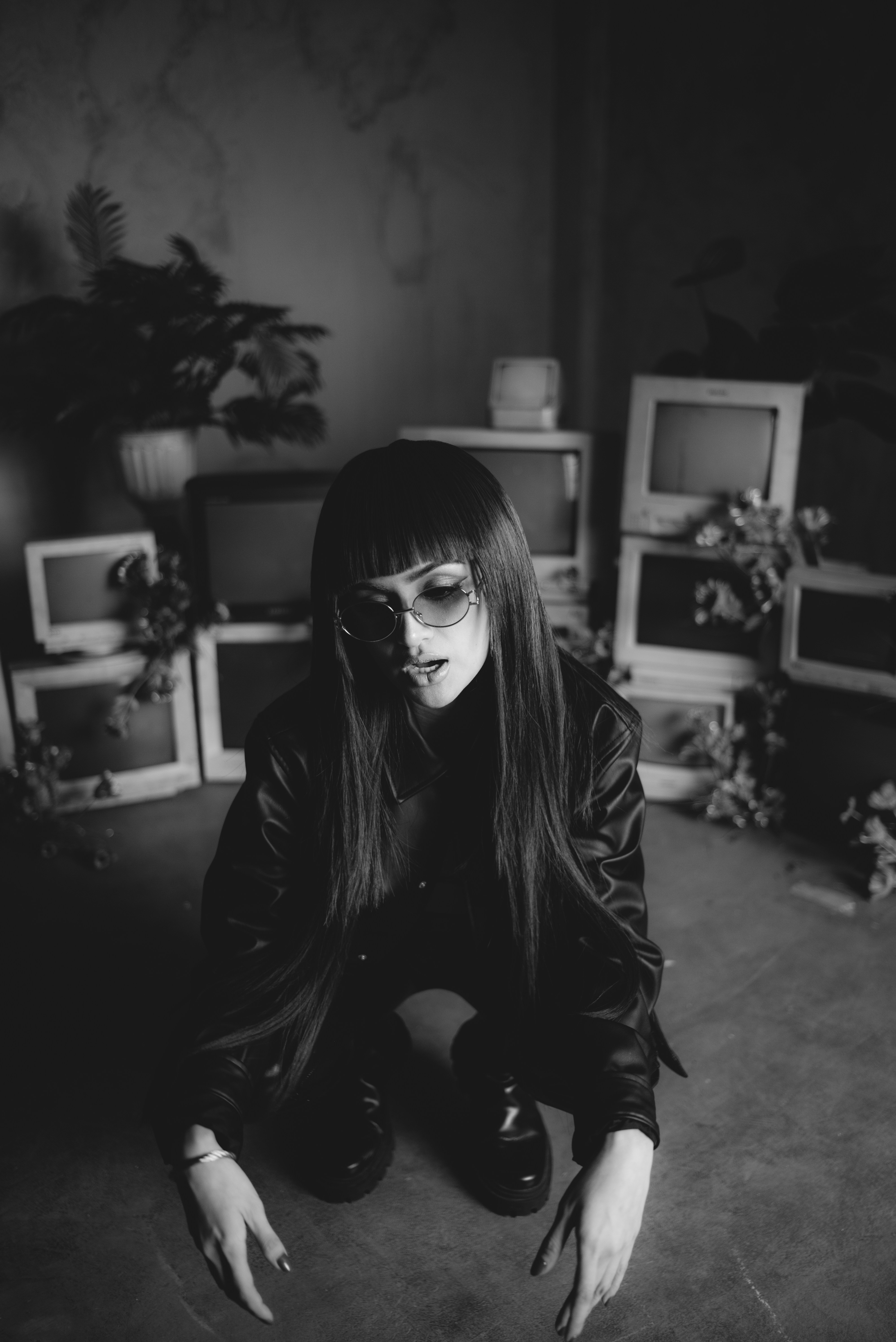 Woman with long dark hair and sunglasses crouching.