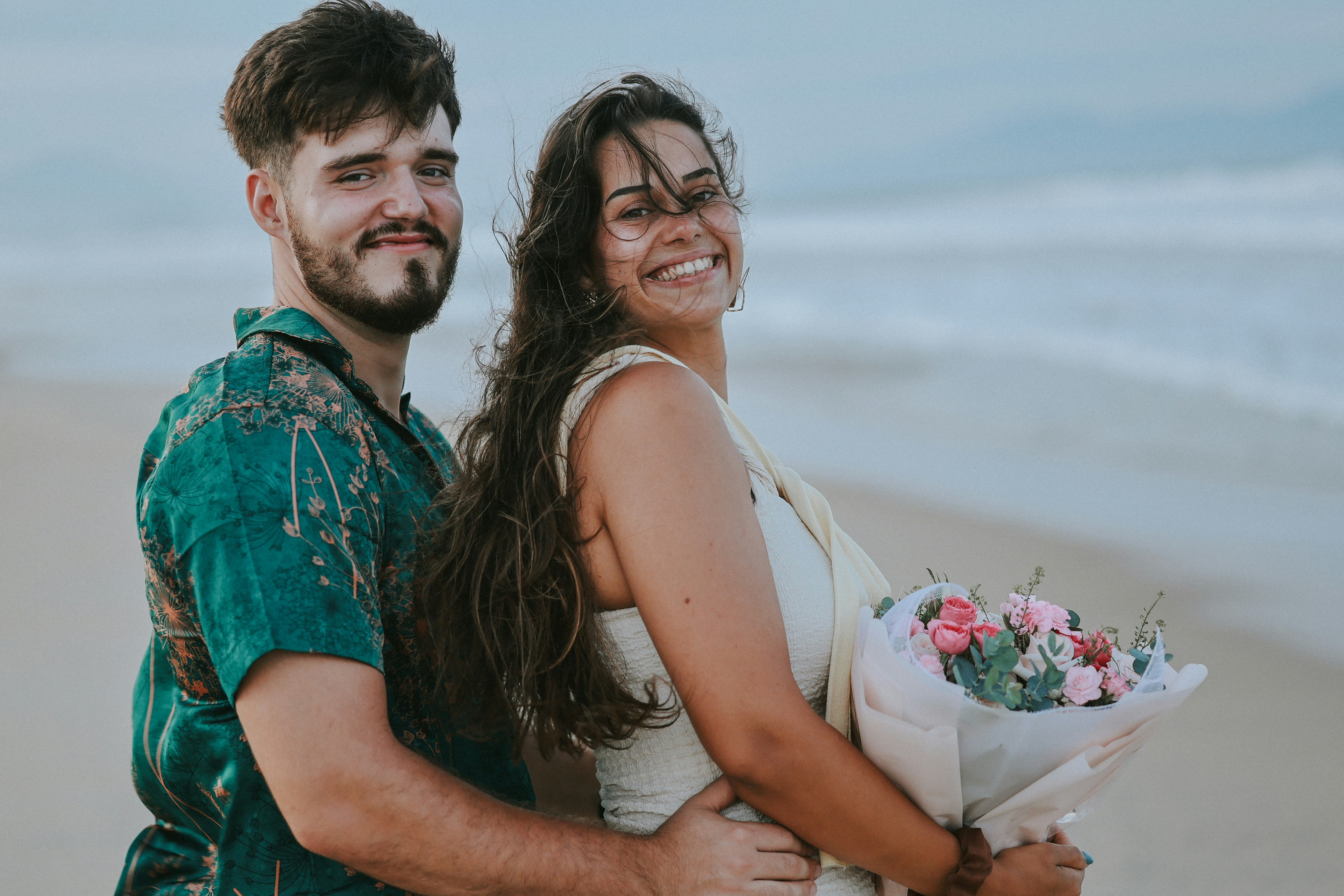 Couple embracing on a beach with a bouquet.
