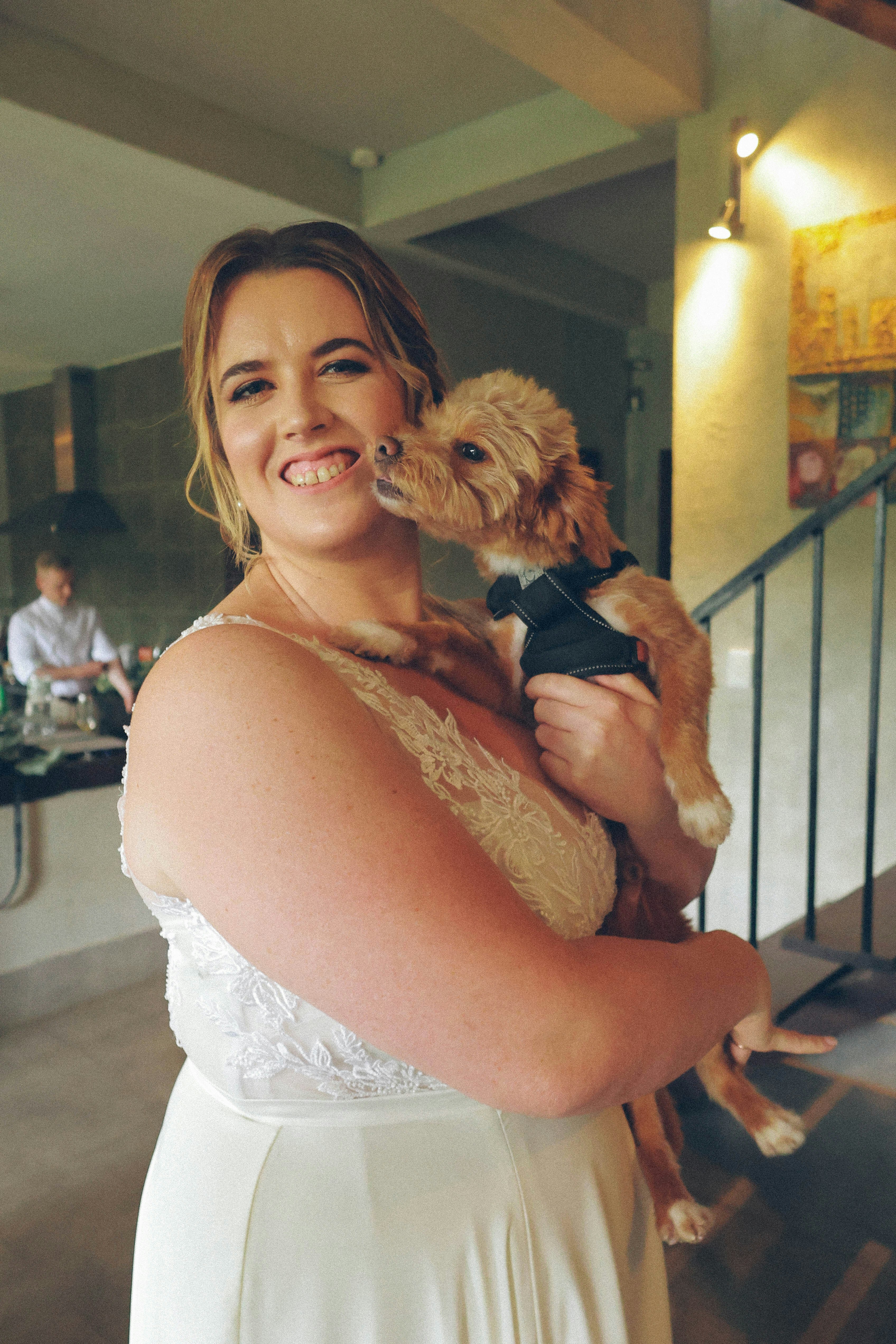 Bride holding a small dog kissing her cheek