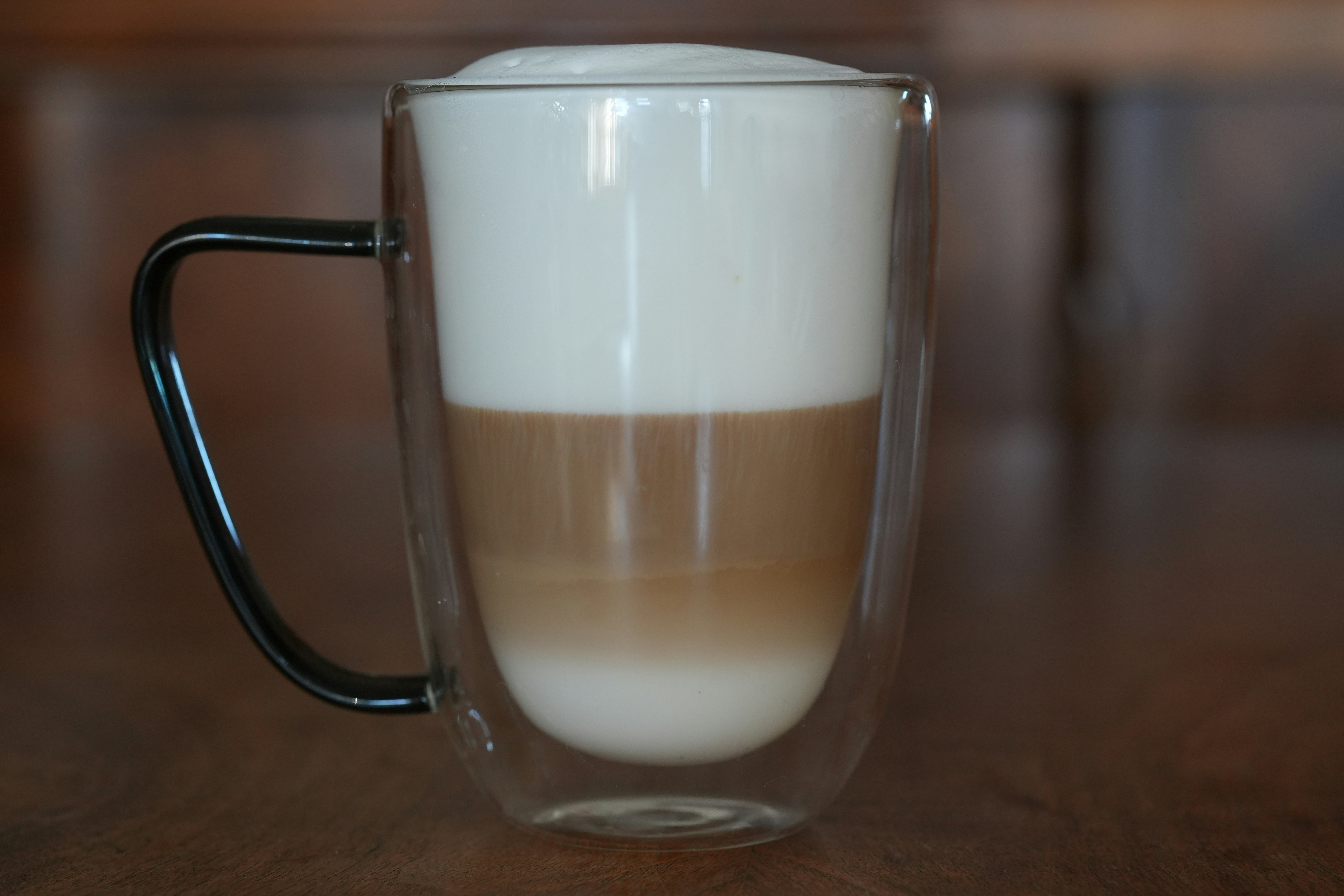 A layered latte with frothy milk in a glass mug.