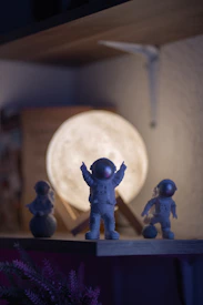 Astronaut figurines in front of a moon lamp on shelf