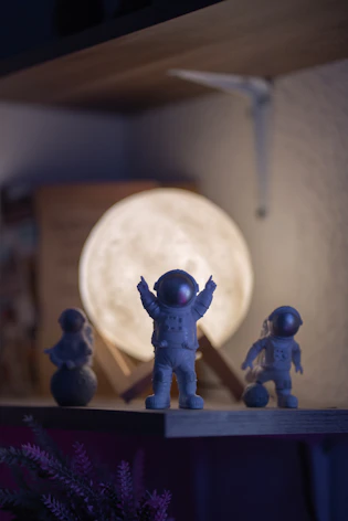 Astronaut figurines in front of a moon lamp on shelf