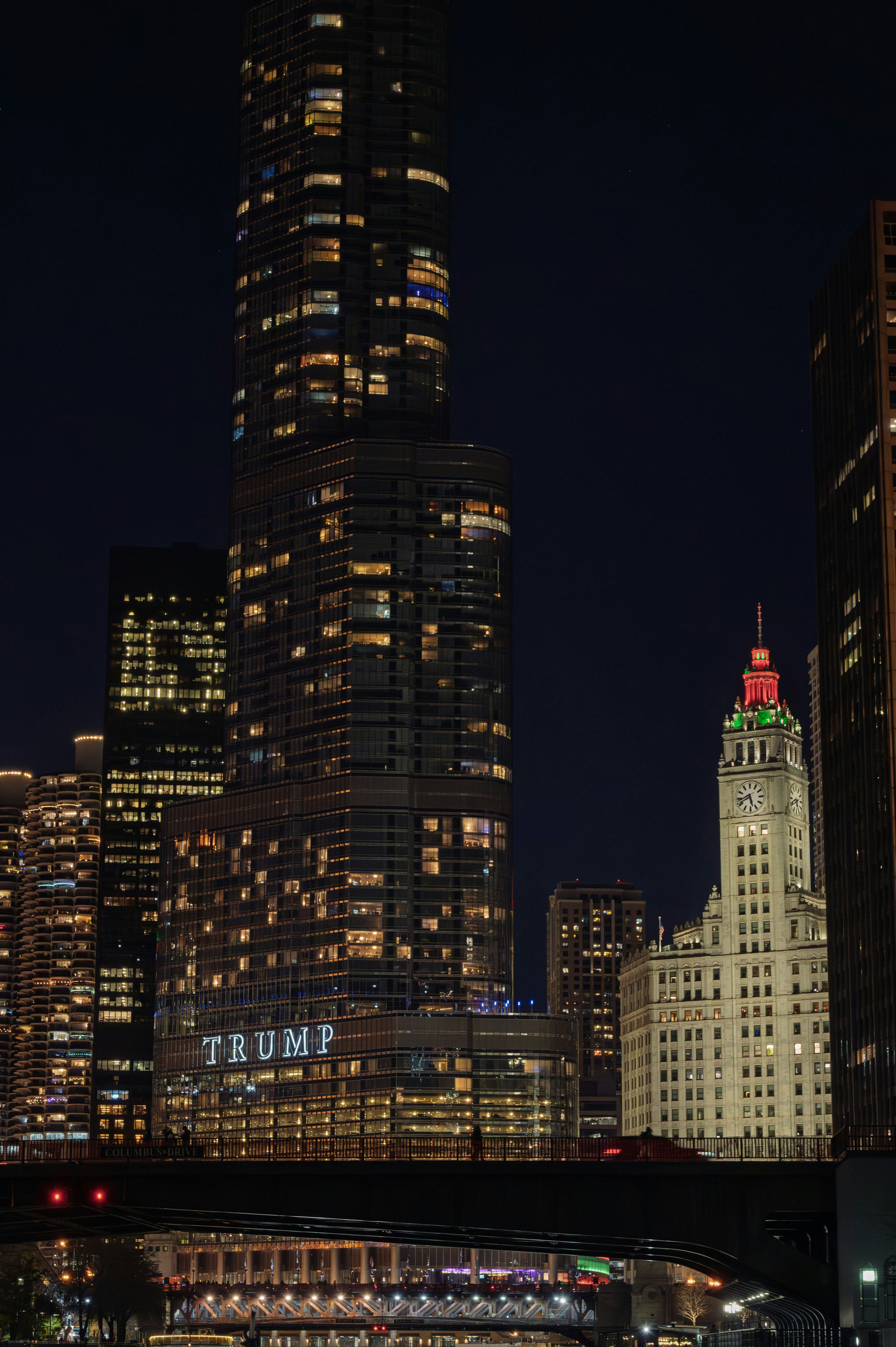 Cityscape at night with illuminated skyscrapers and bridge.