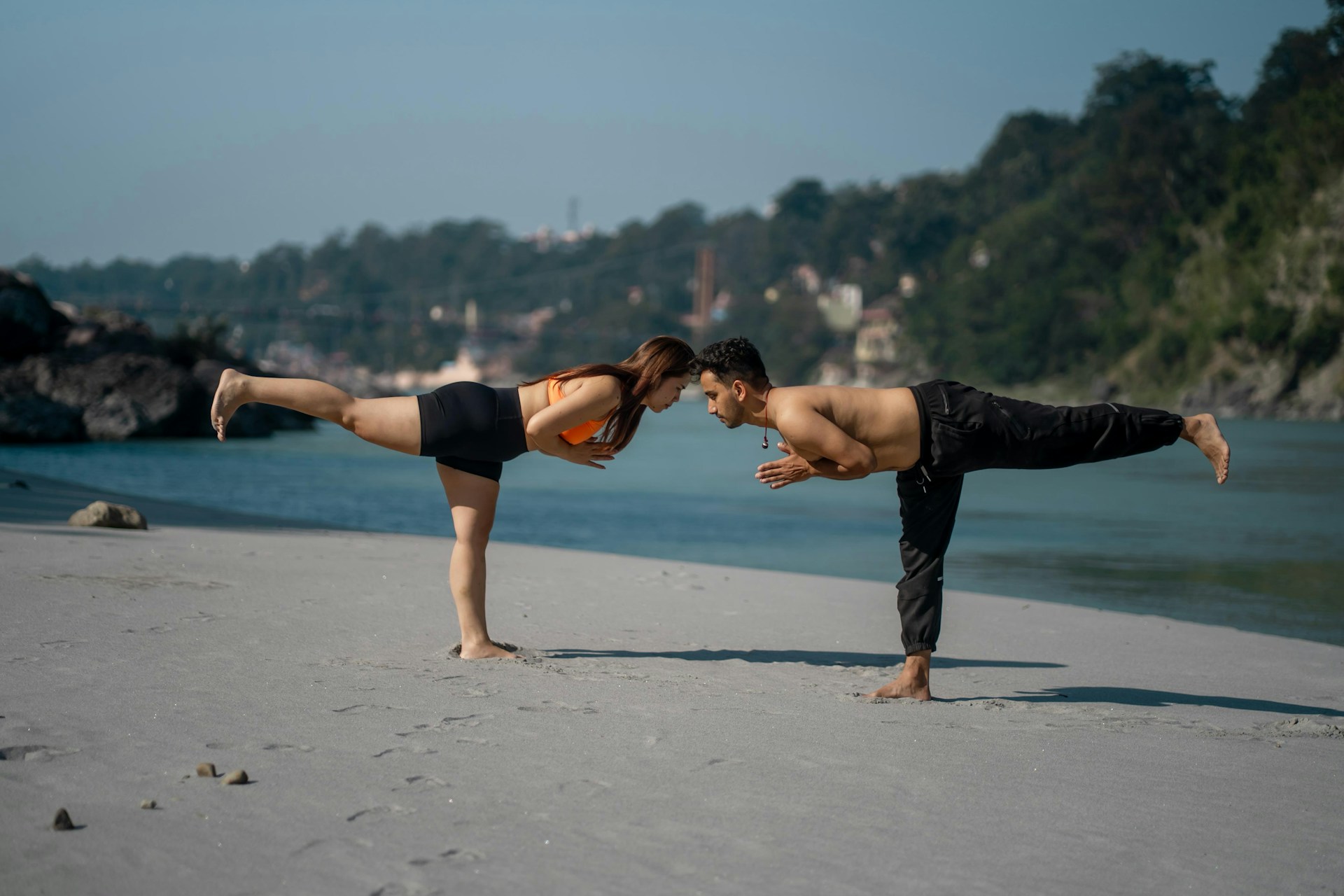 Couple doing yoga on a sandy beach by the water.