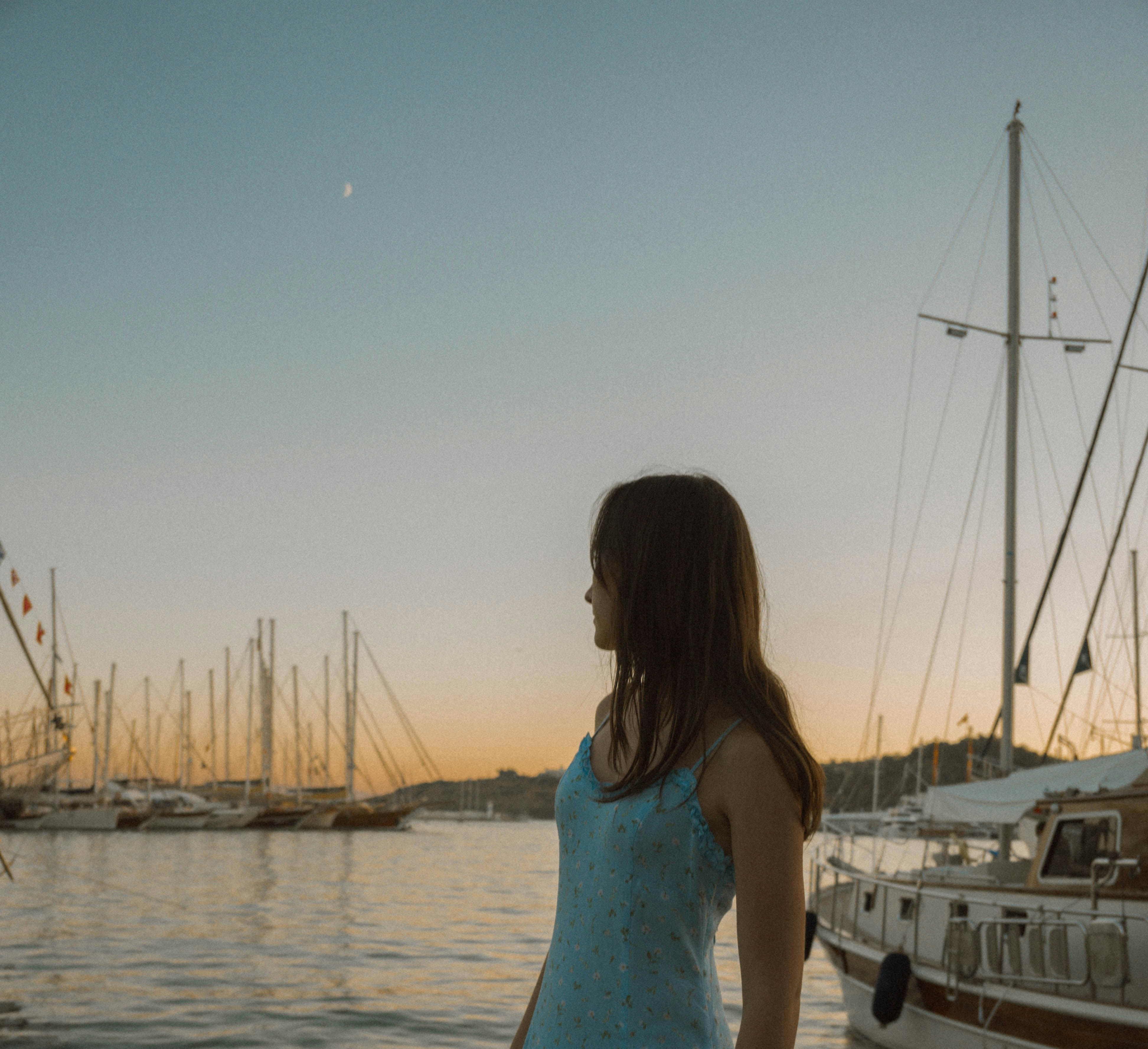 Woman in blue dress by boats at sunset