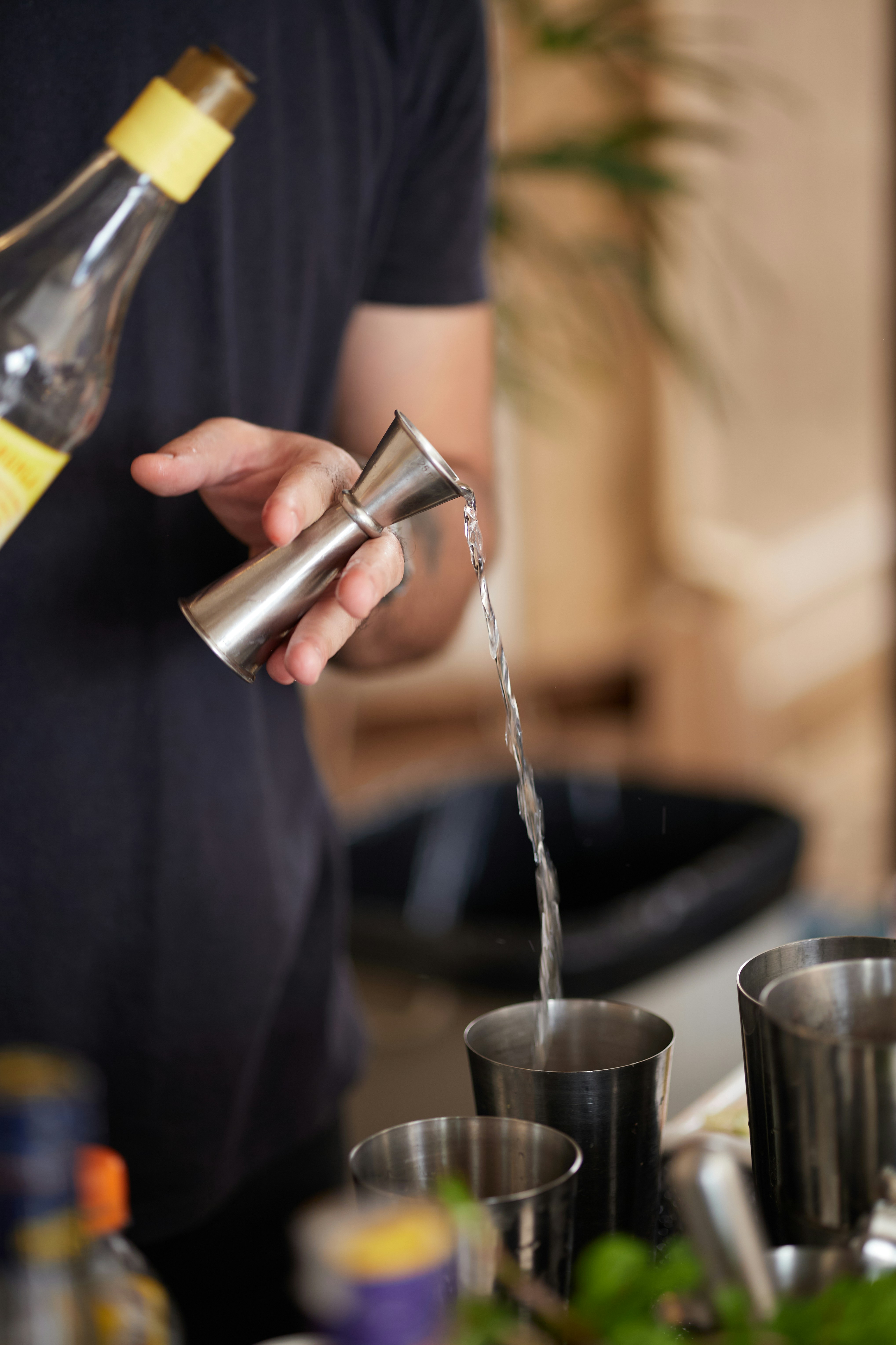 Bartender pouring liquid from bottle into jigger.