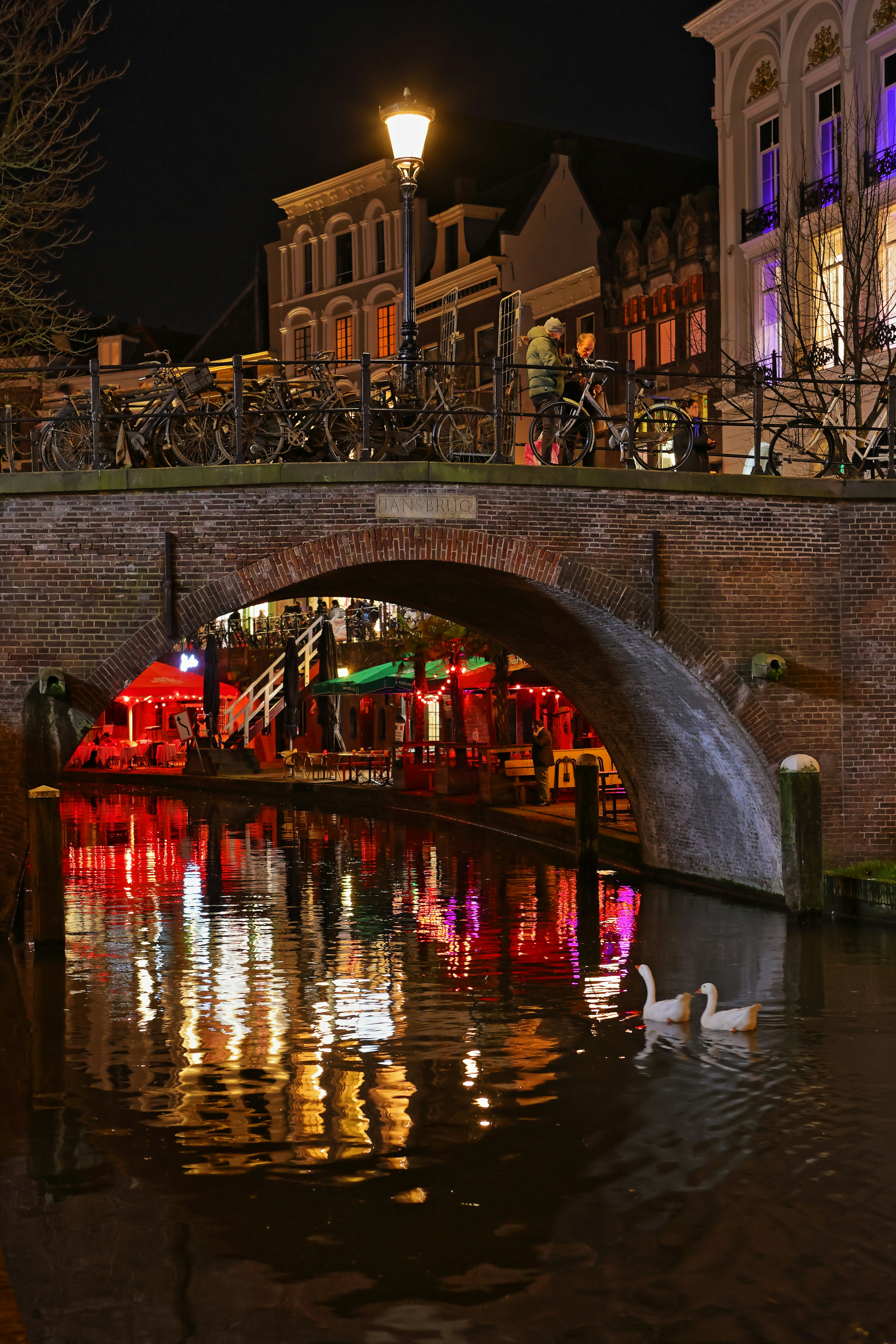 Canal da cidade à noite, com ponte iluminada e reflexos.