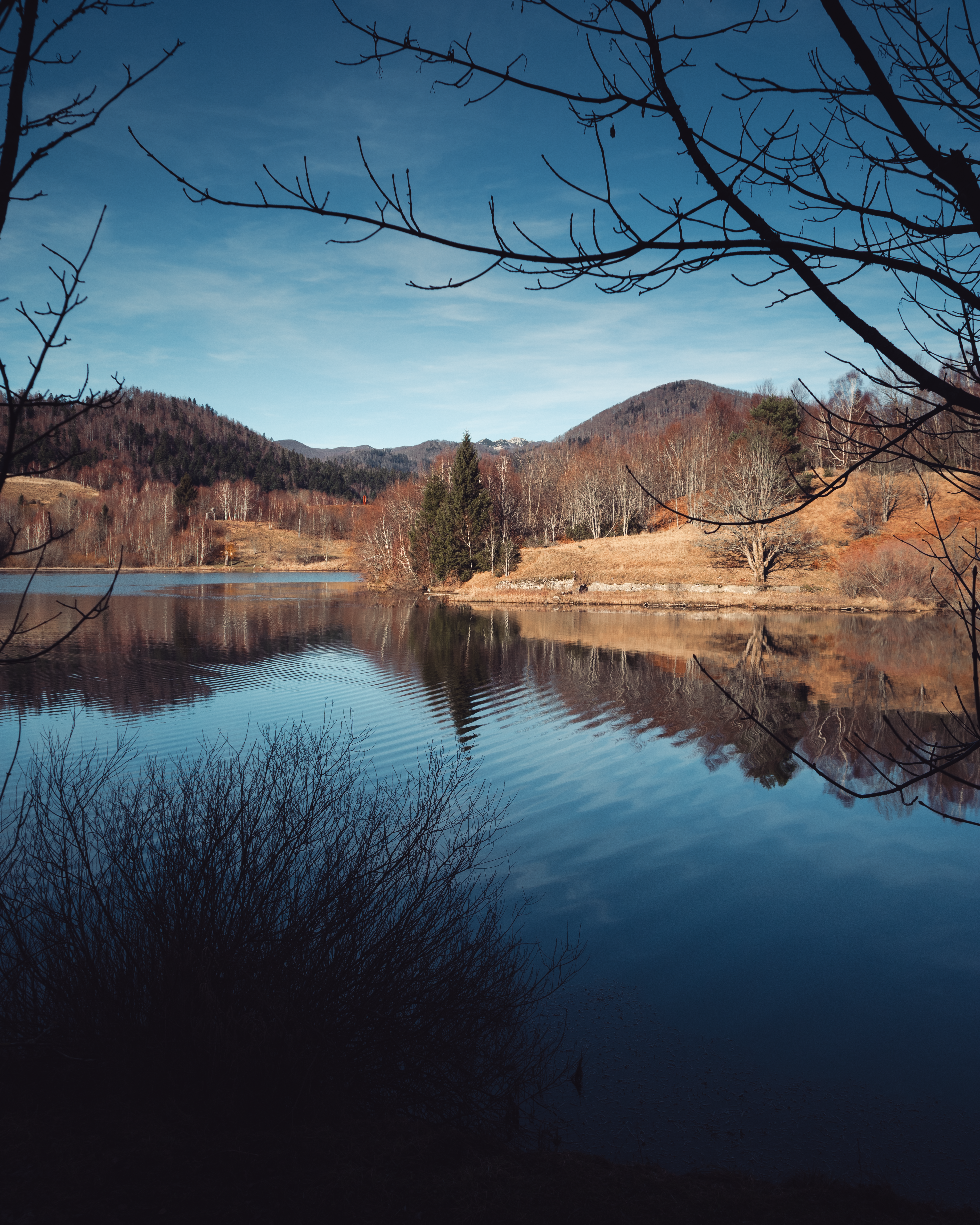 Calm lake reflecting trees and hills under blue sky
