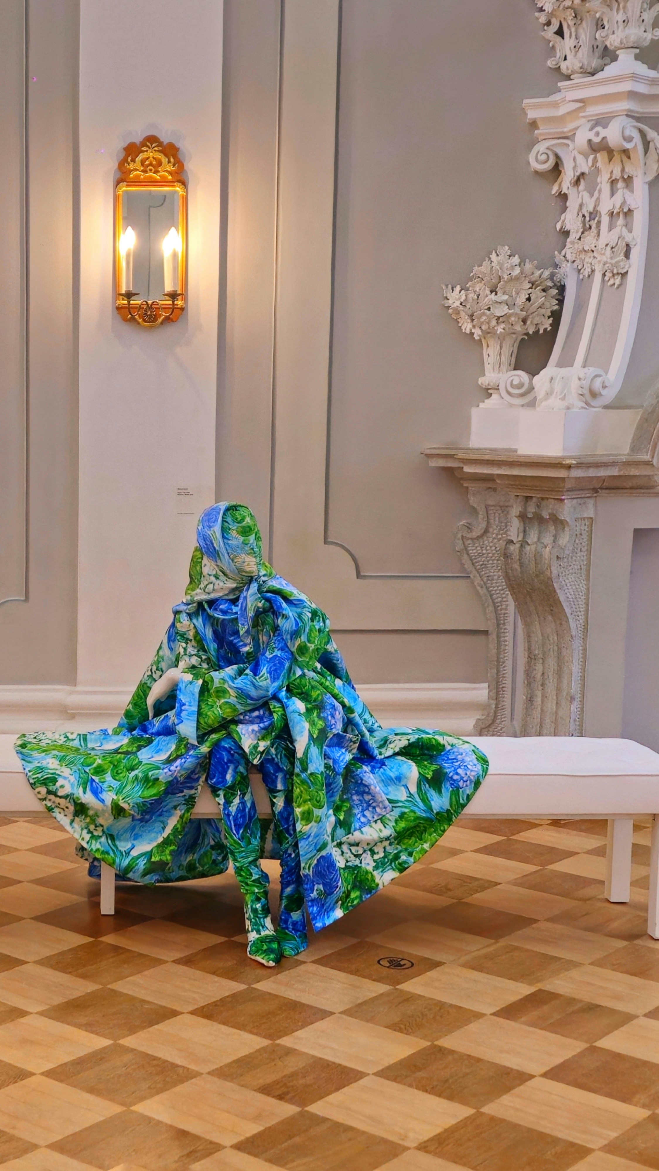 Mannequin in vibrant floral outfit on white bench.