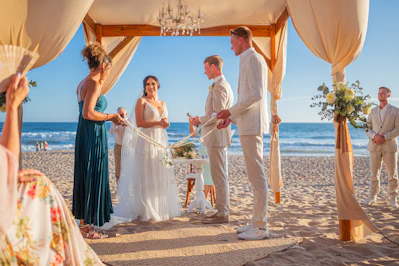 A wedding ceremony on a sunny beach with ocean backdrop.
