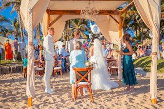 Wedding ceremony on a sandy beach with guests watching.