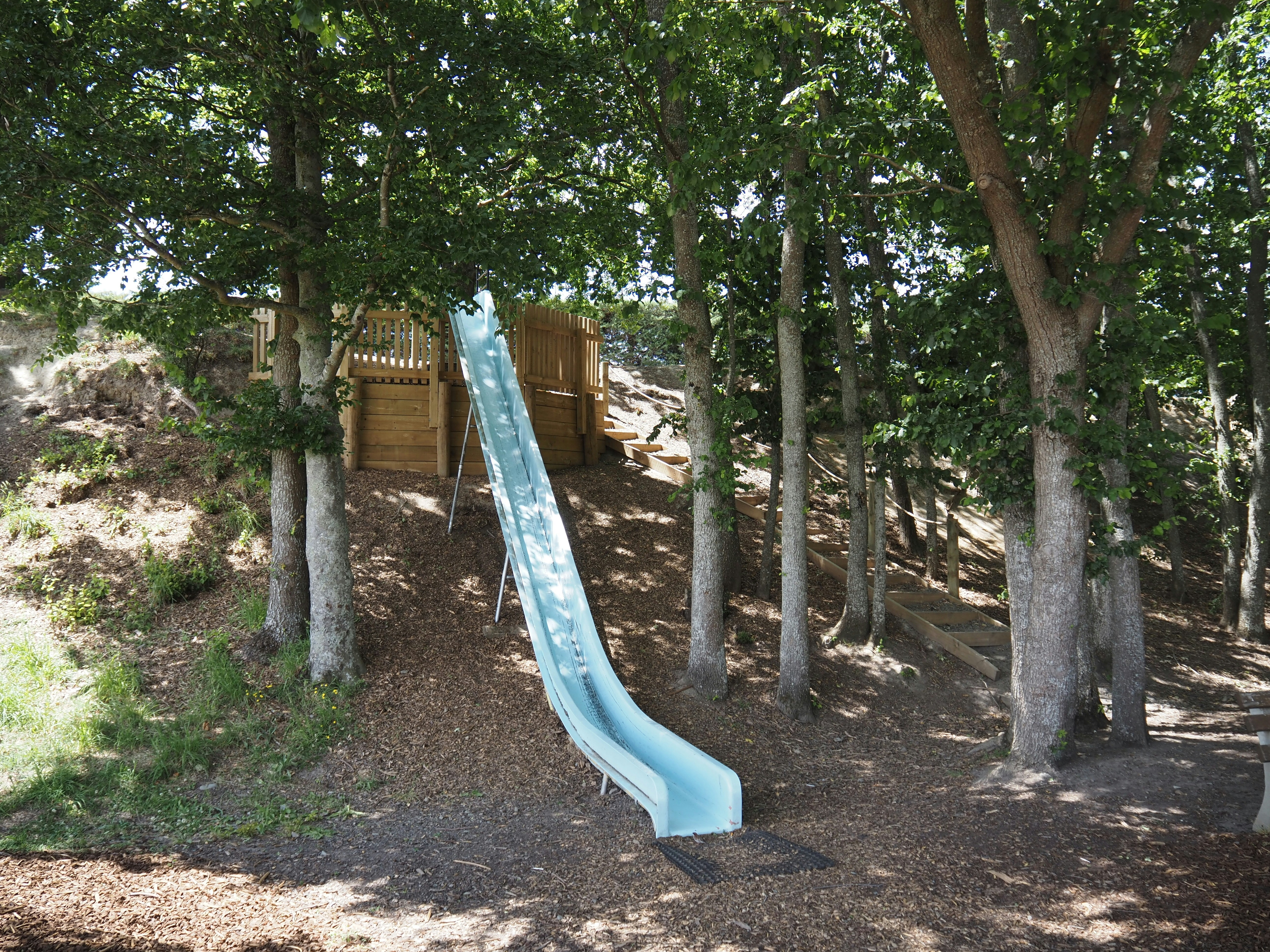 Un tobogán azul en un área de juegos boscosa con árboles.