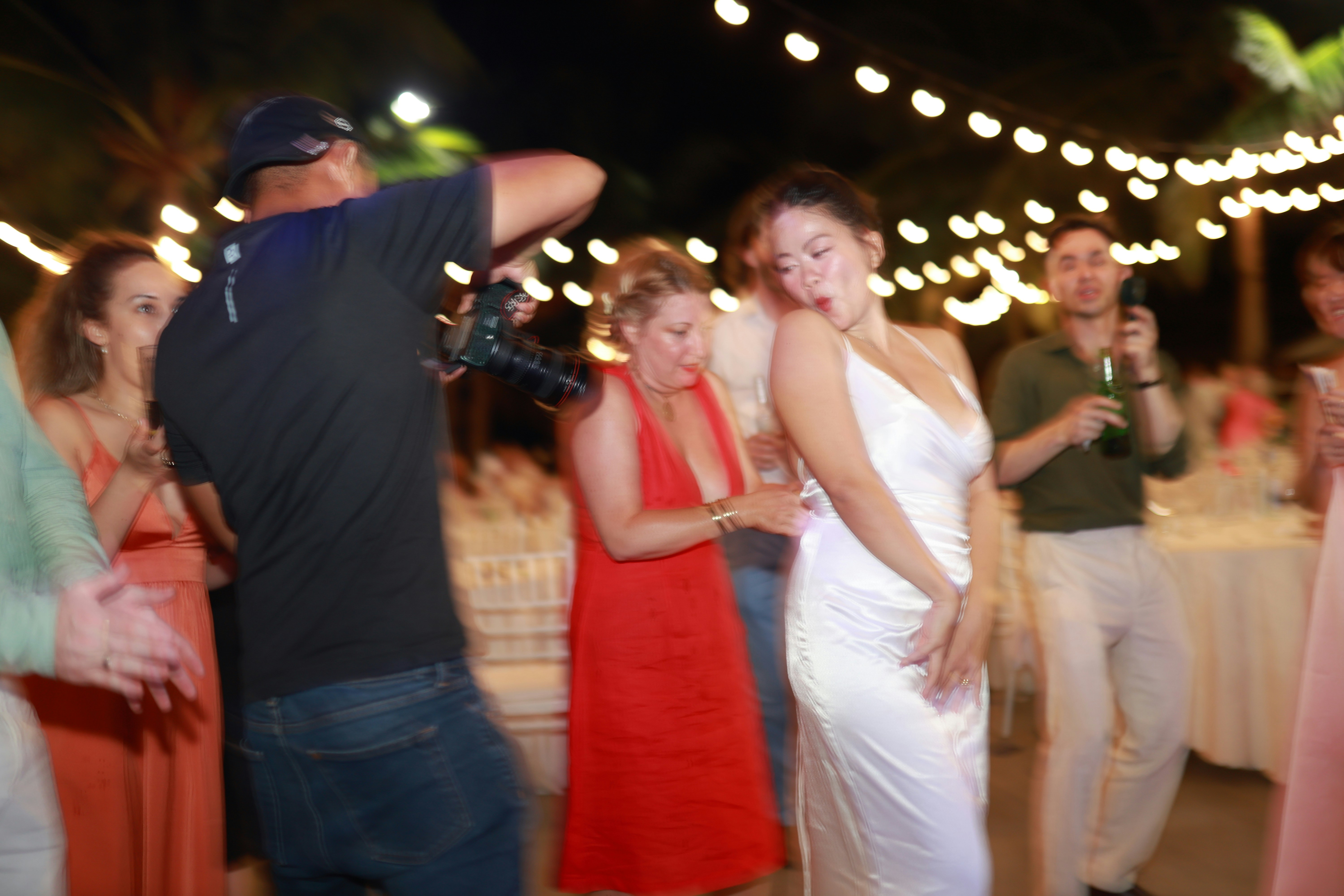 Woman in white dress dances at party with string lights.