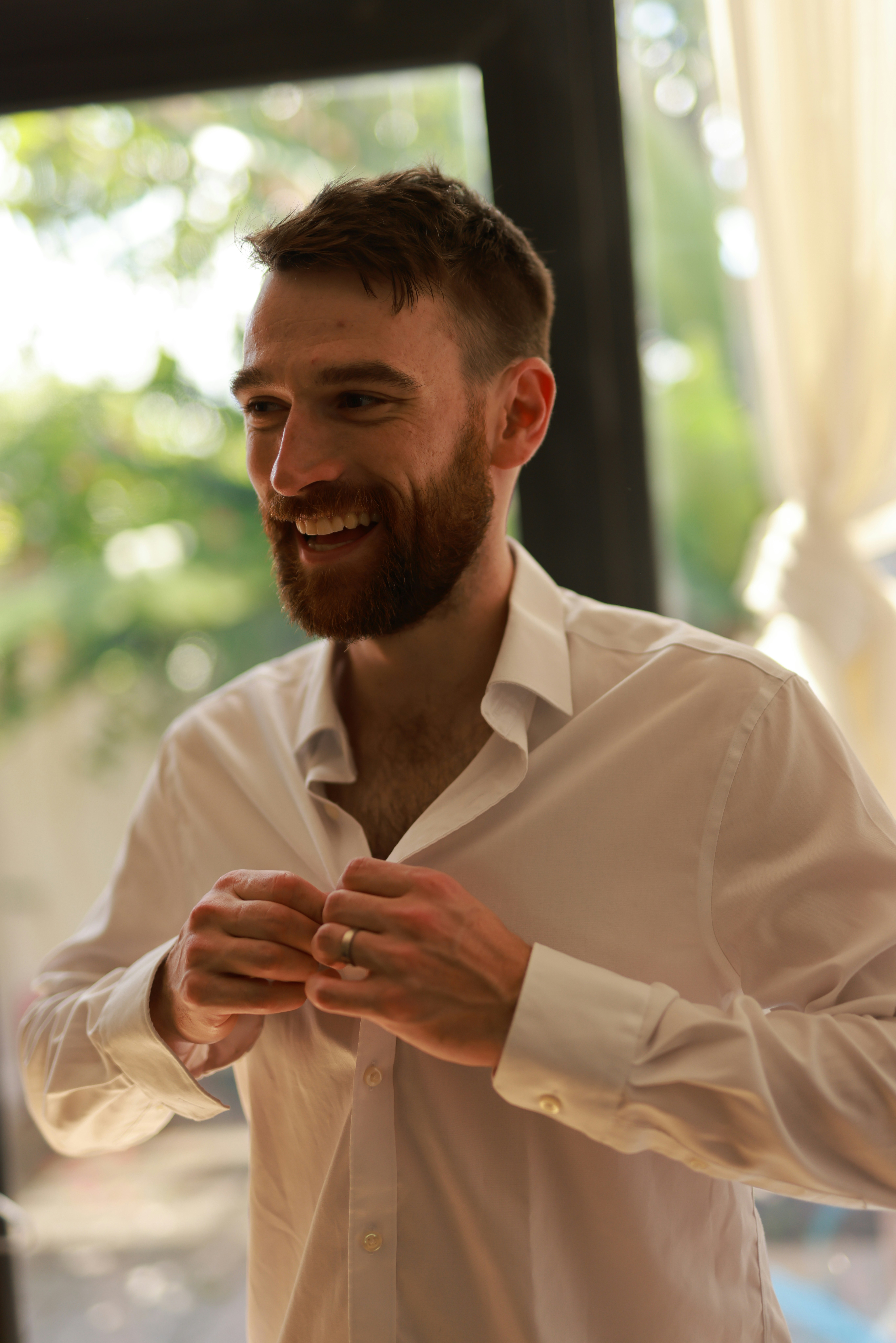 Man in white shirt buttons up with a smile