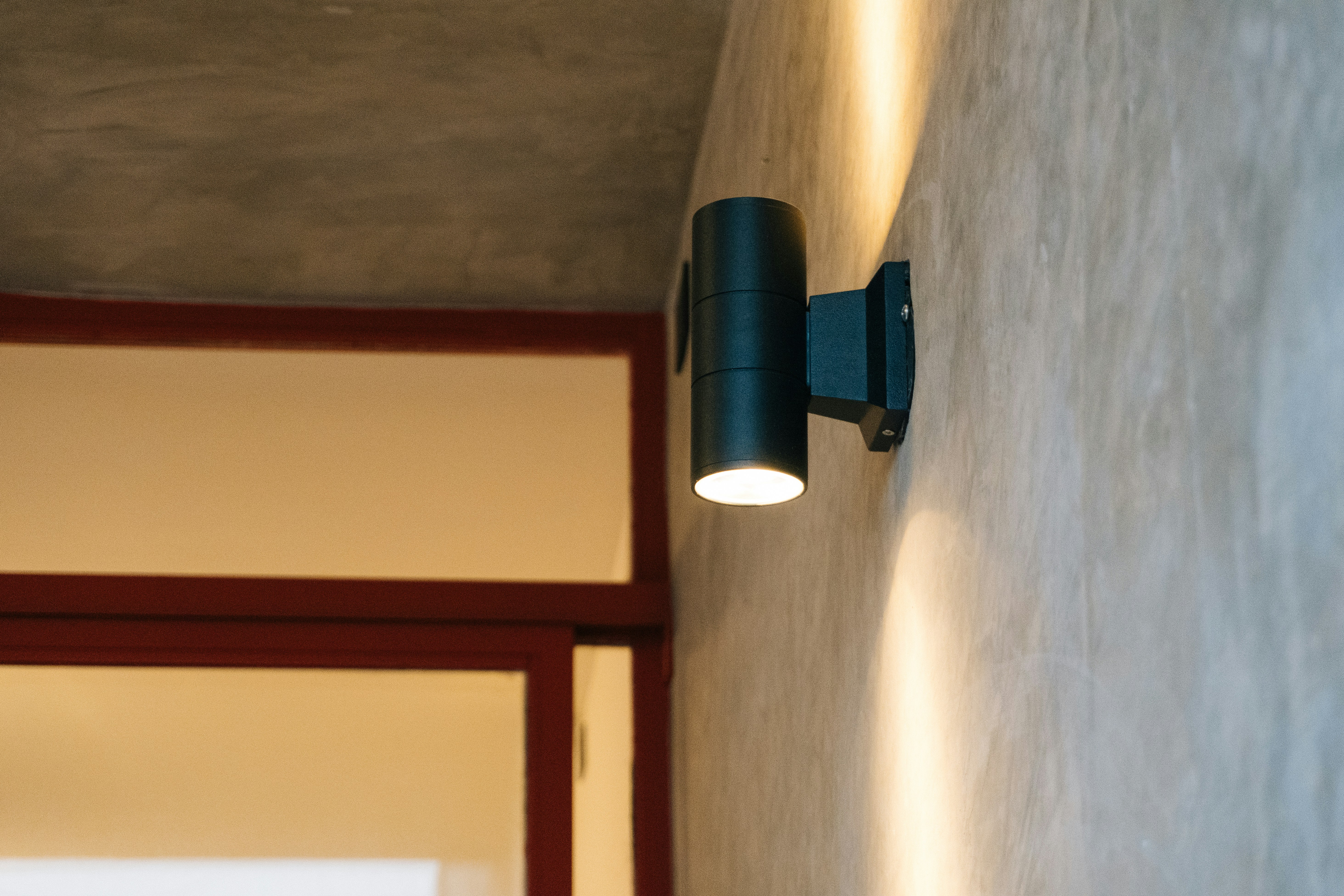 A modern black outdoor wall light illuminates concrete wall.