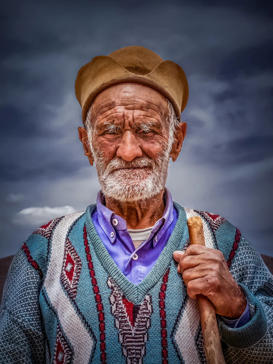An elderly man with a weathered face, holding a staff