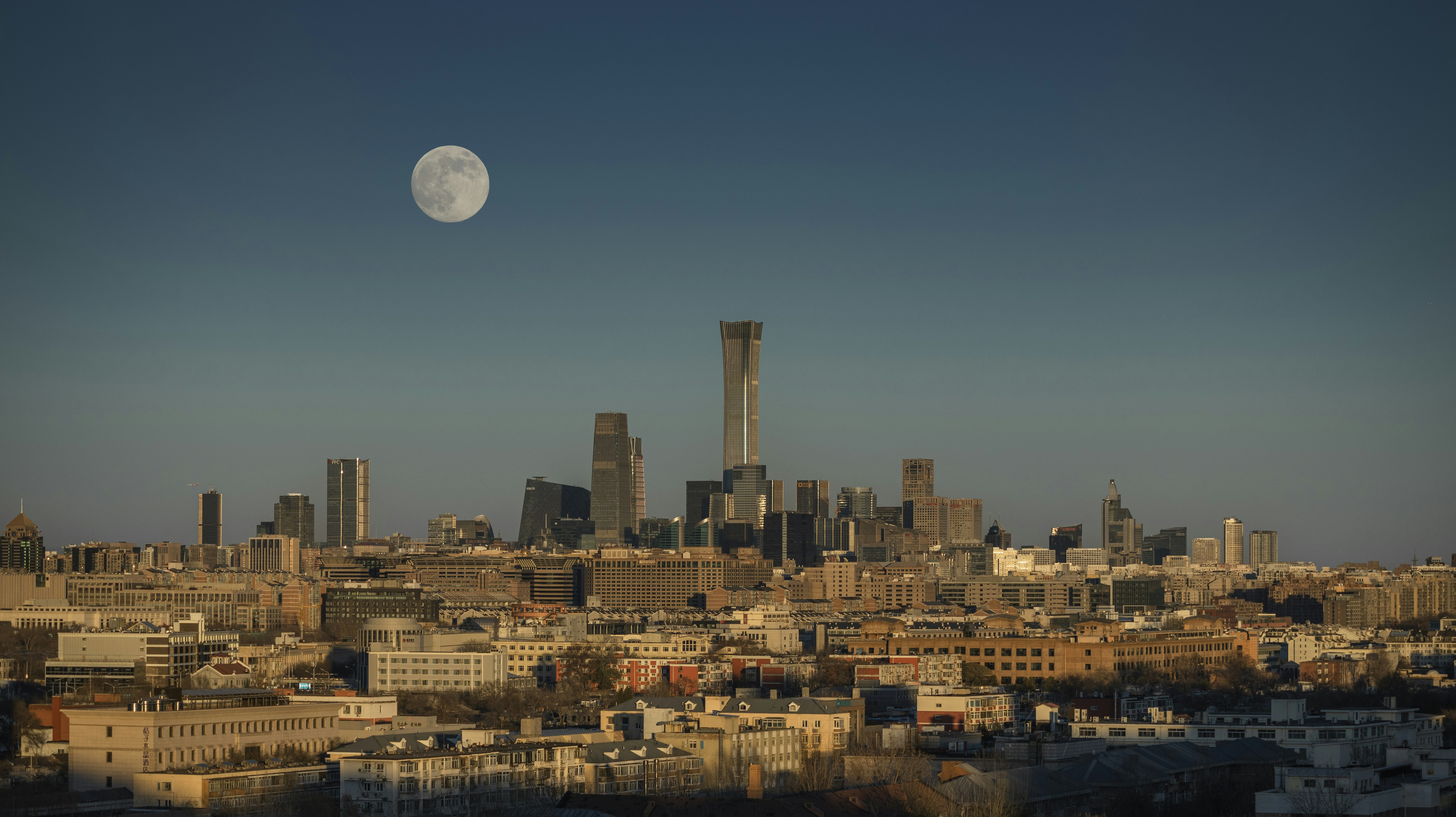 Moon over a modern cityscape at dawn.