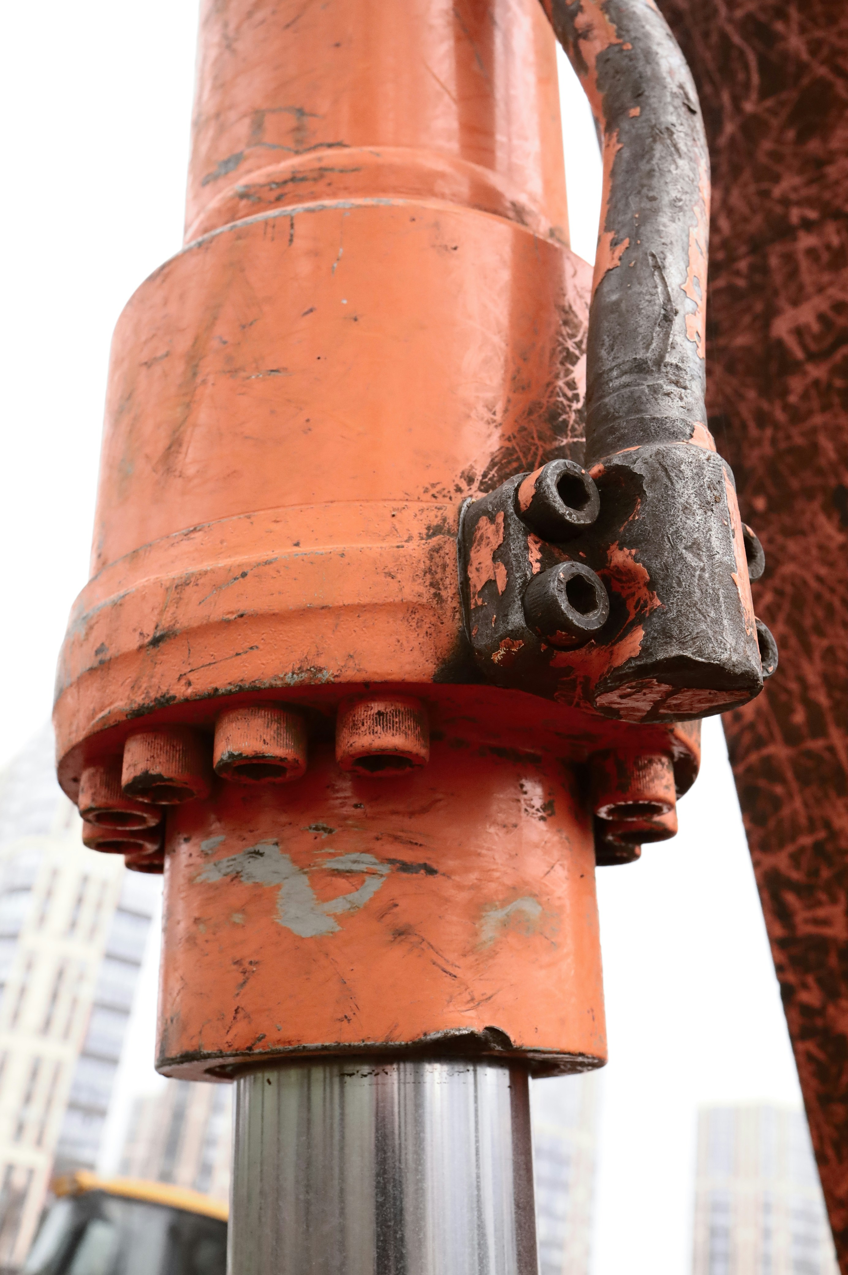 Close-up of an orange hydraulic cylinder with bolts.