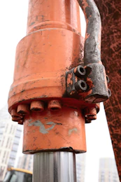 Close-up of an orange hydraulic cylinder with industrial bolts