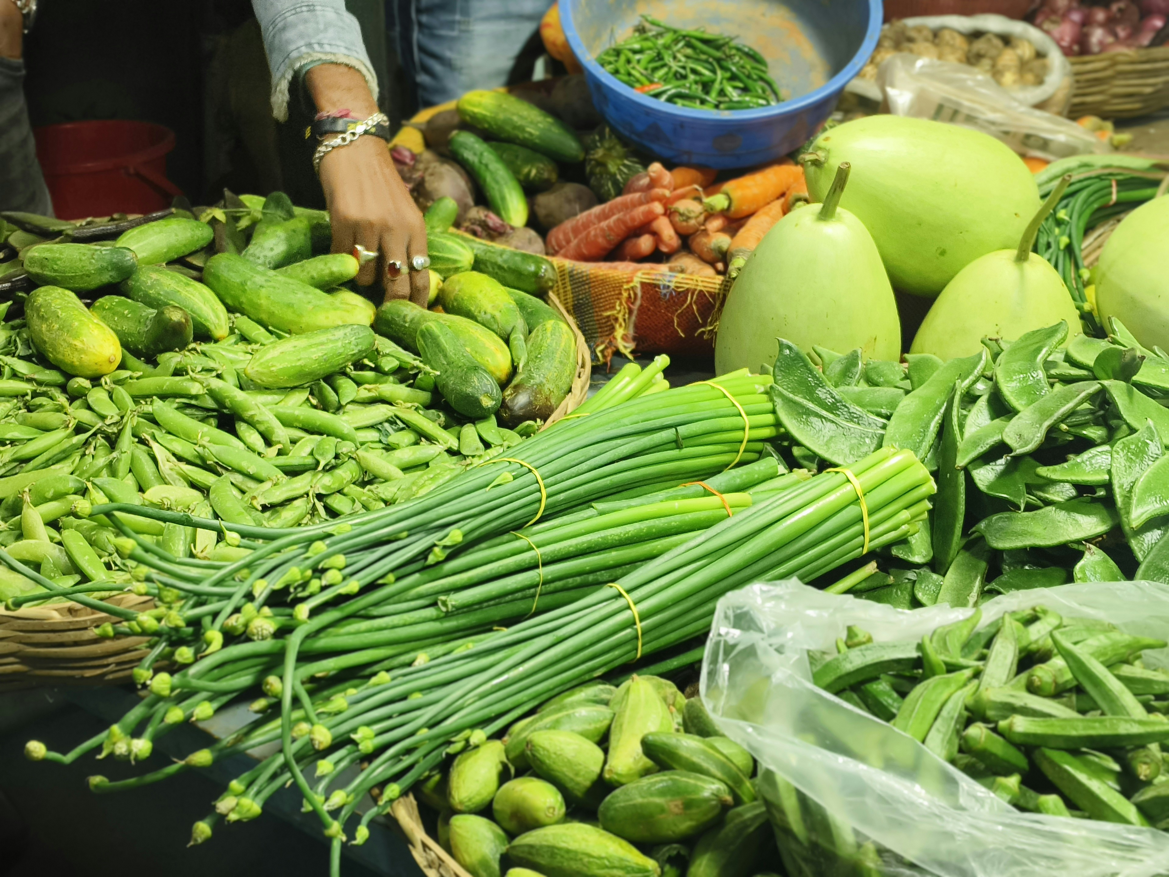 Pazar tezgahında veya rustik bir mutfak masasında bir araya getirilmiş taze, yerel ve mevsimlik sebzelerle meyveler; ekonomik ve sağlıklı beslenmeyi simgeliyor.