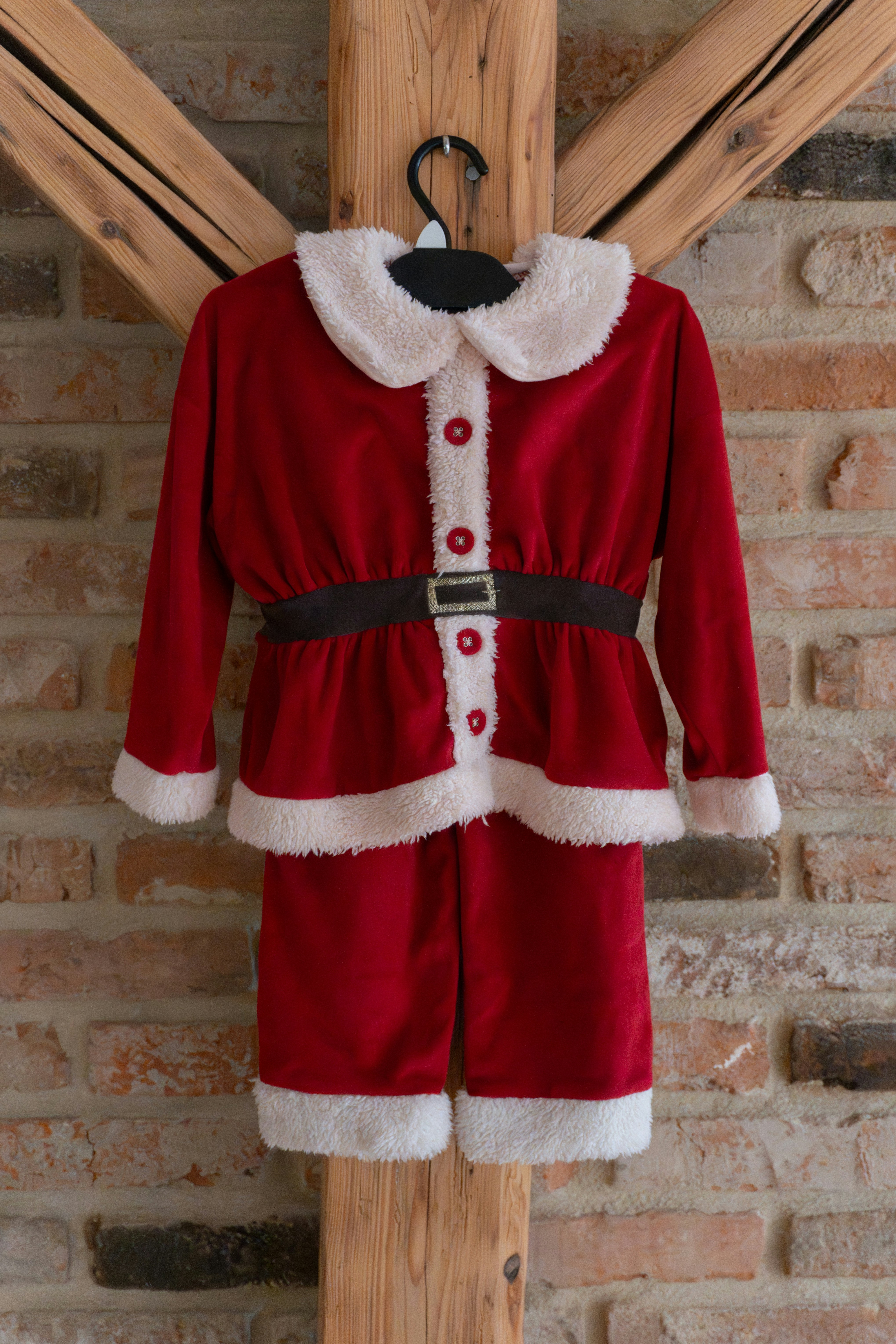 A child's santa claus costume hangs on a wooden beam.