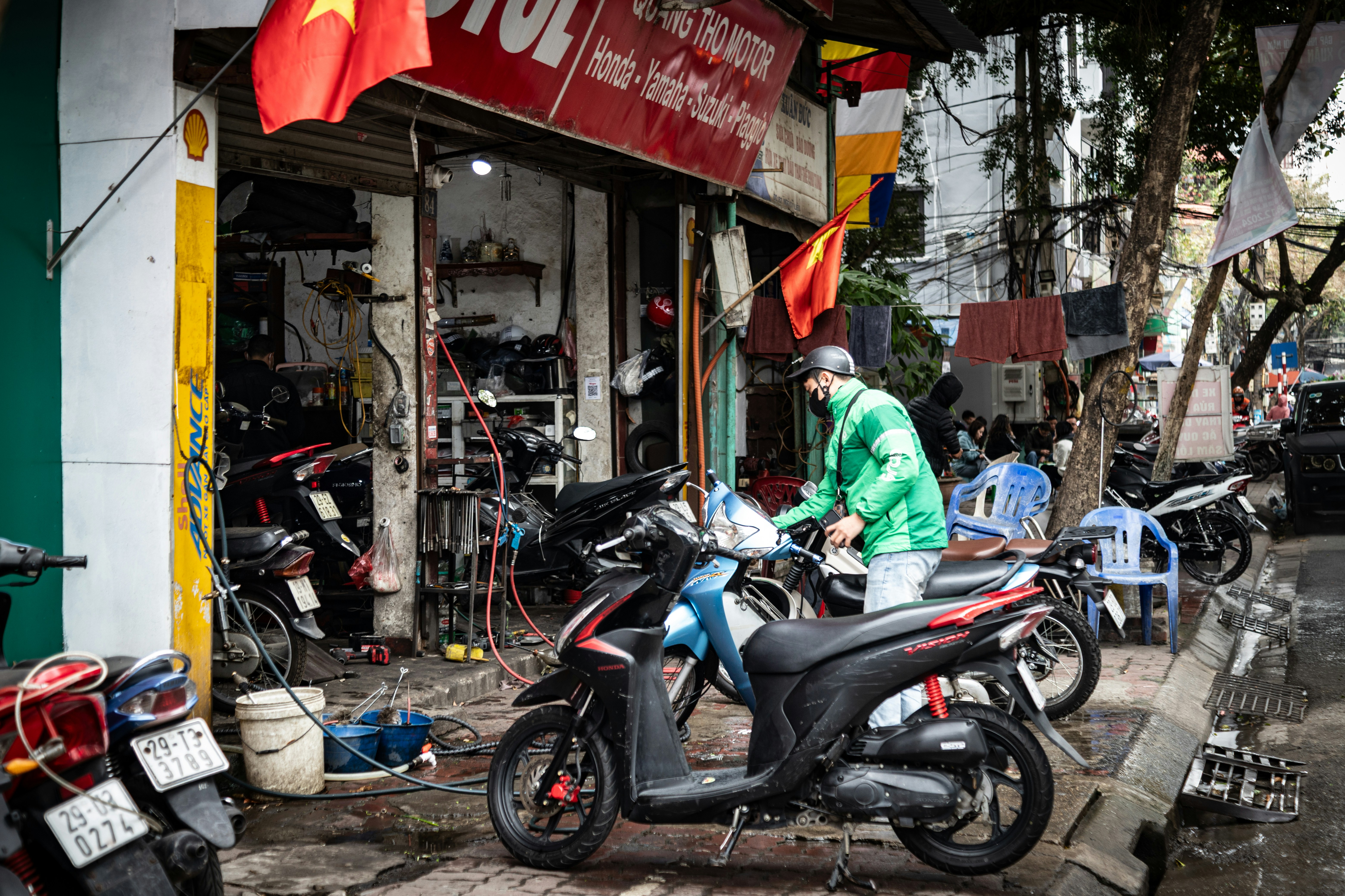 Man in green jacket works on motorcycles outside shop.