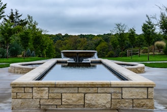 A formal stone fountain with water and surrounding greenery