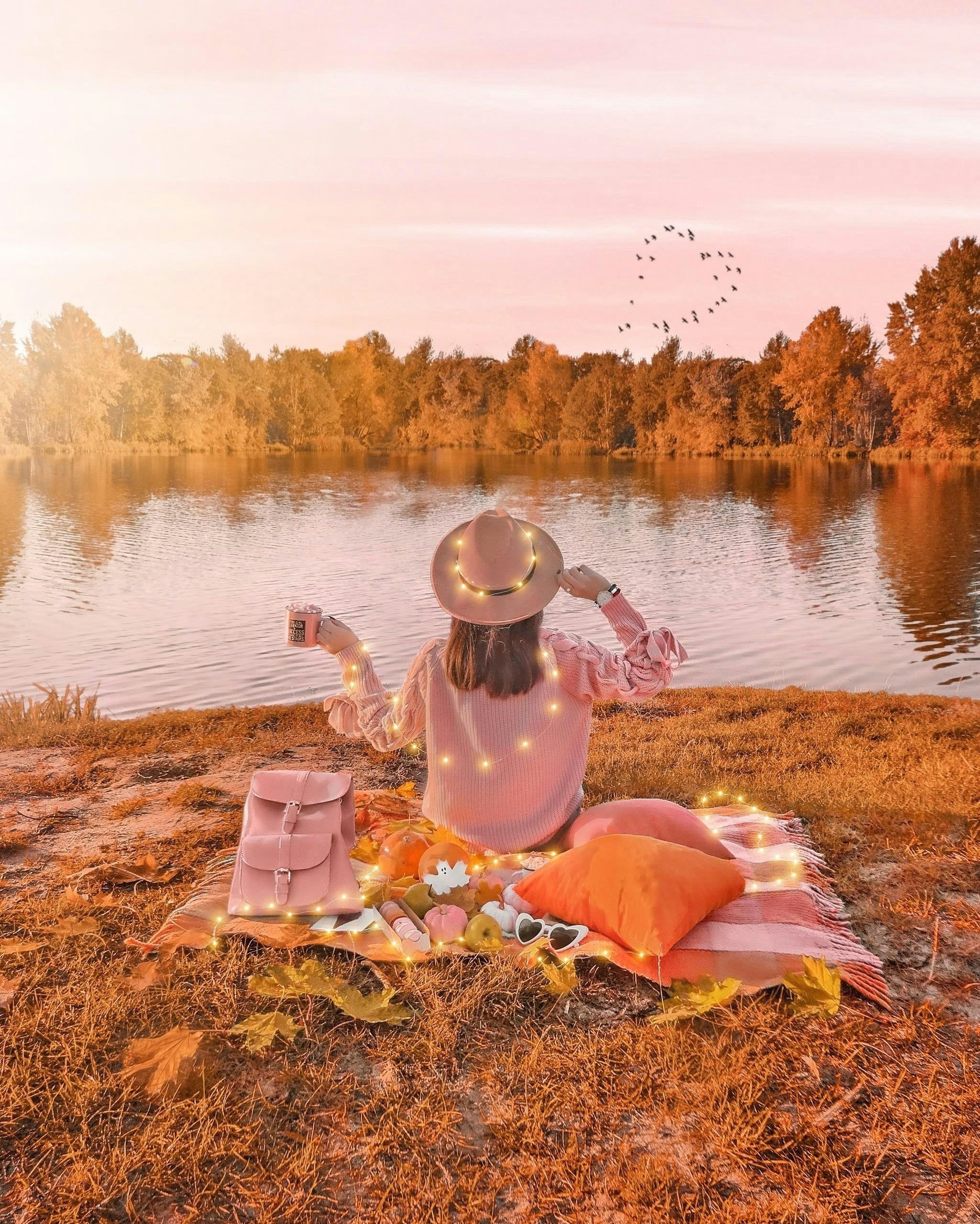 Woman having a picnic by a calm lake at sunset.