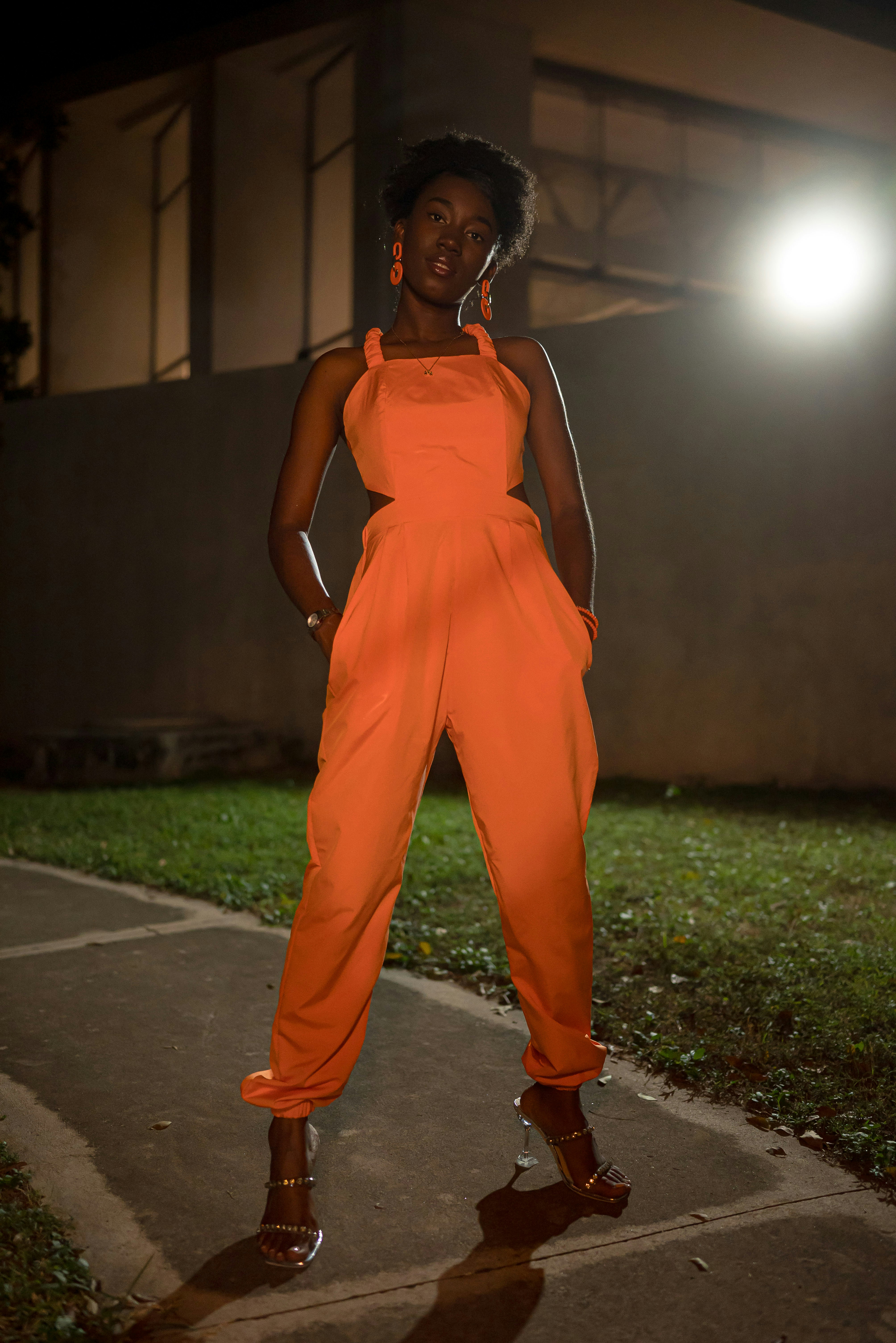 Woman in bright orange jumpsuit standing outside at night.