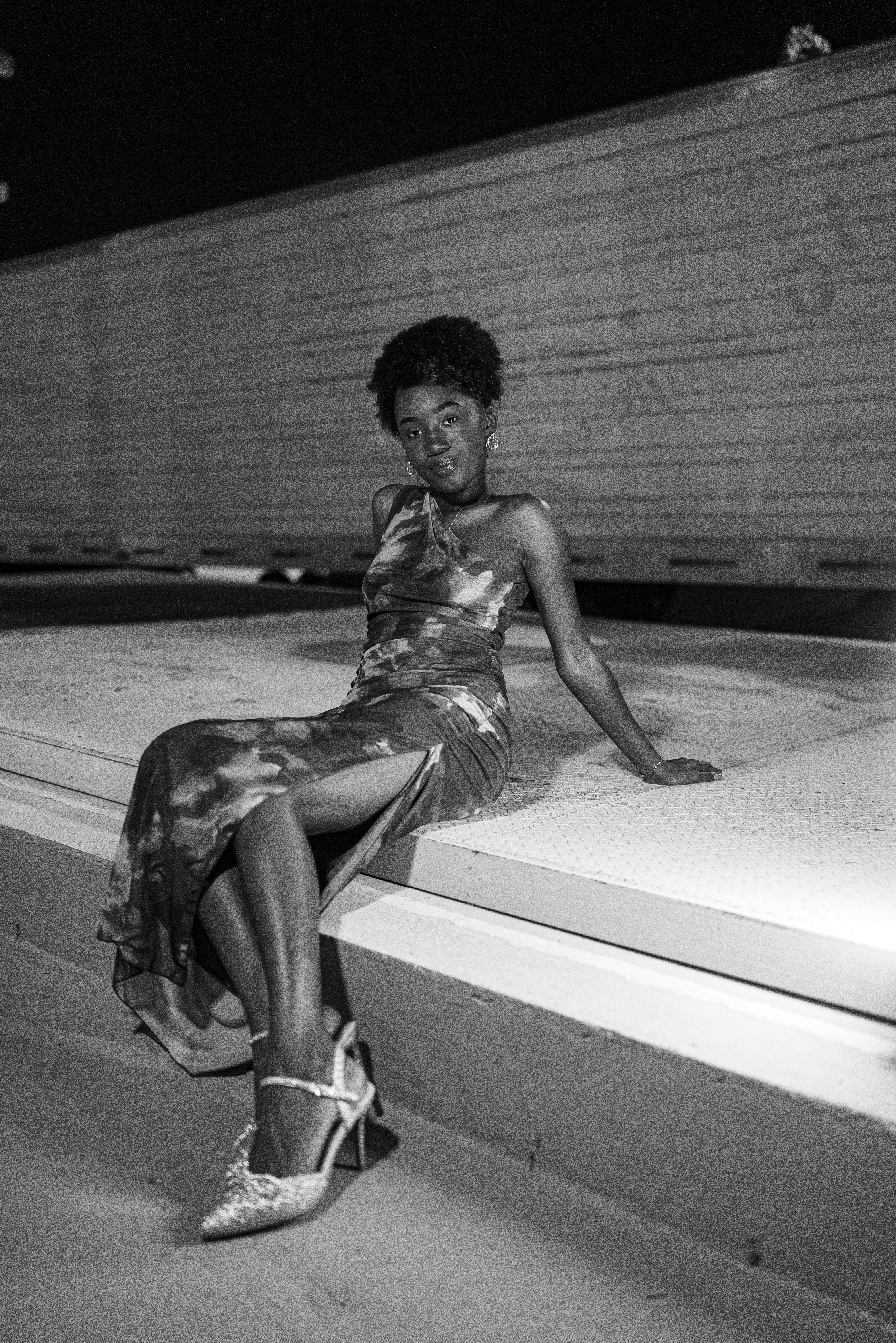 Woman in a patterned dress and heels sitting.