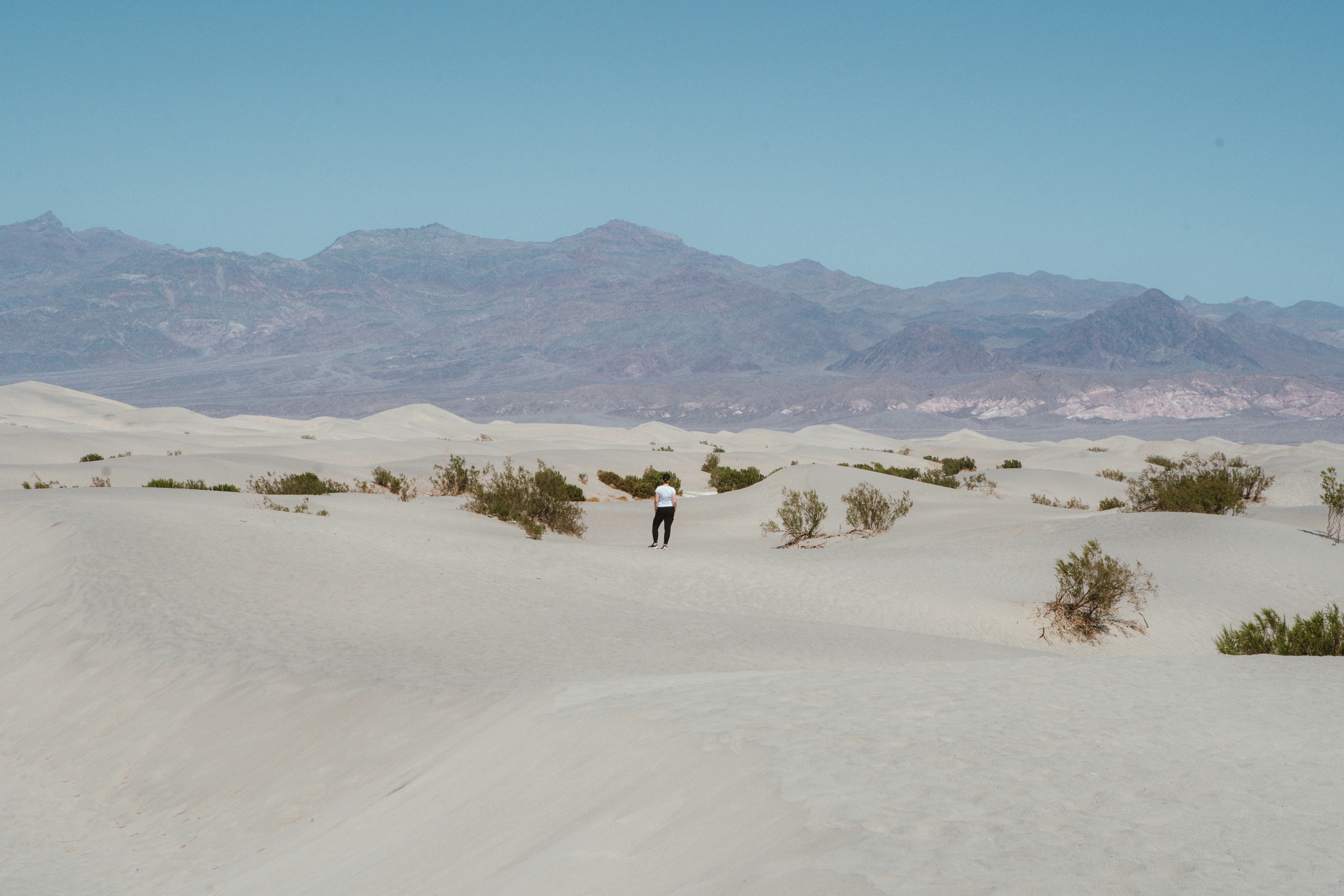 A lone person walks across vast sand dunes.