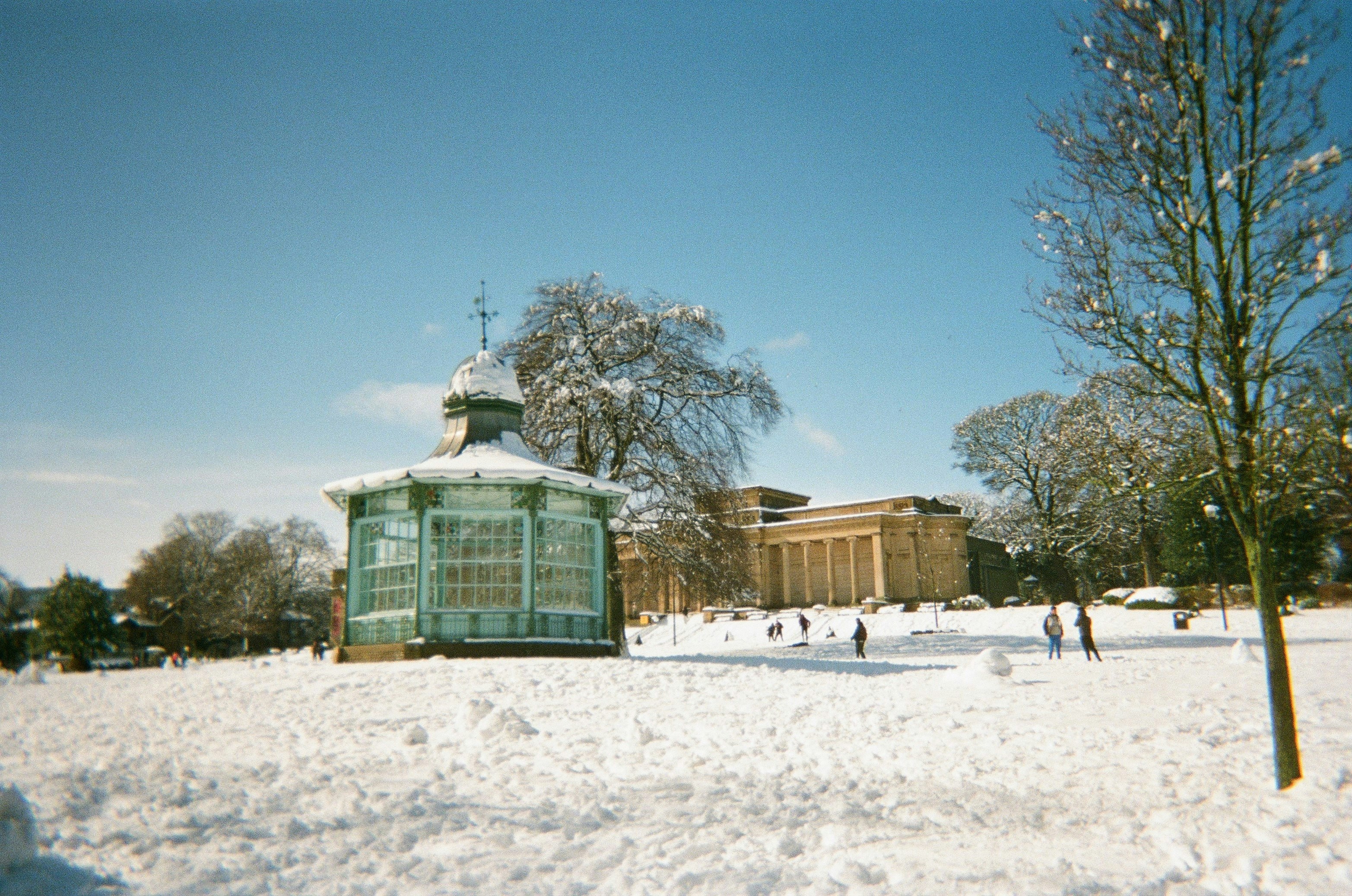 Snow-covered park with a gazebo and building.