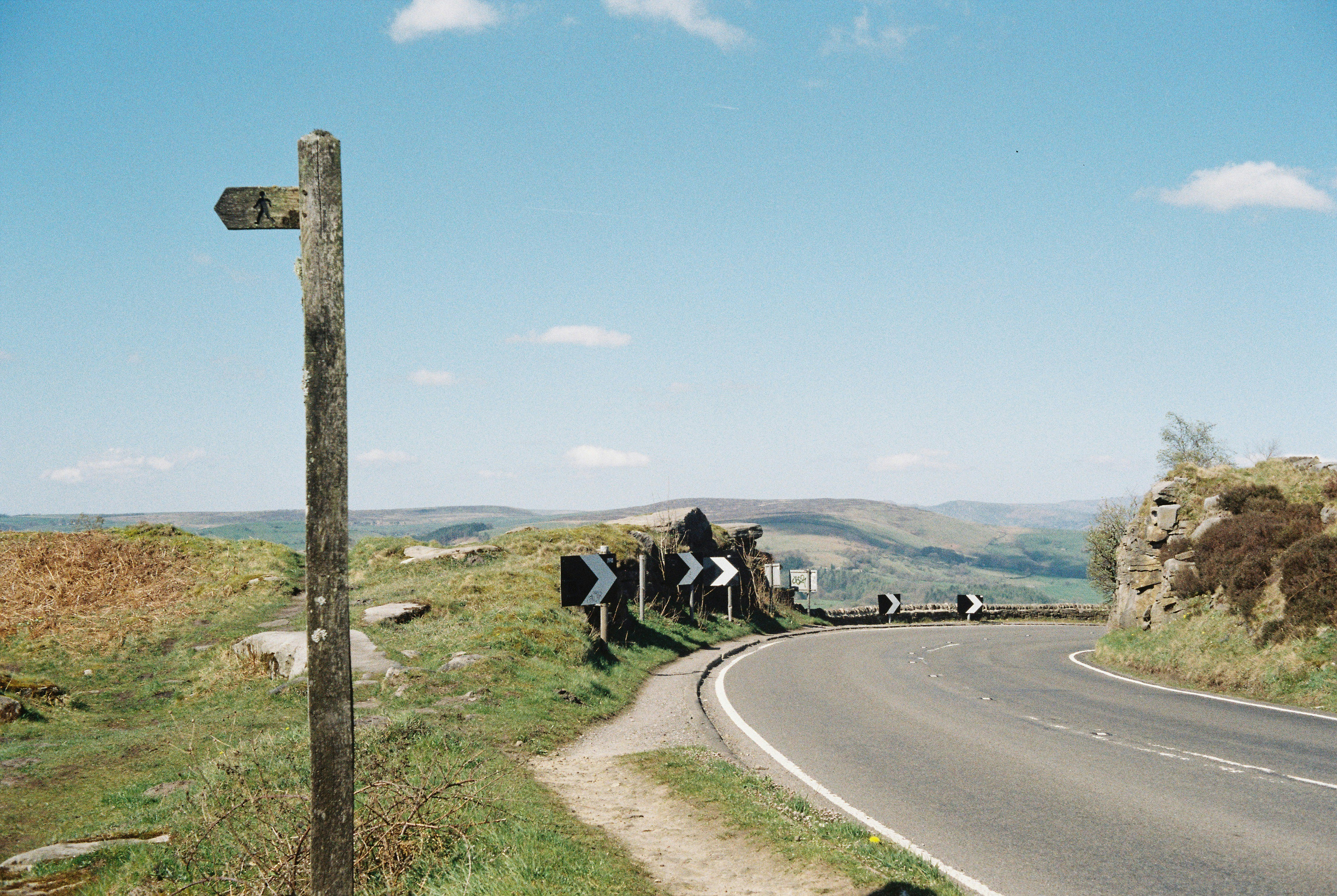 Wooden signpost beside a winding road with hills.